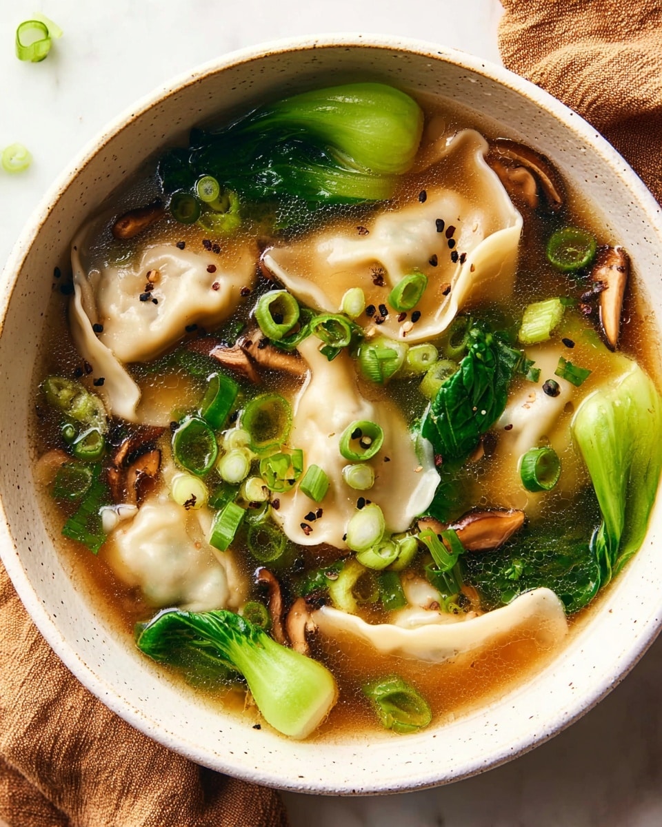 A white bowl filled with clear brown broth holds multiple pale dumplings with a soft, slightly wrinkled texture near the edges. Scattered on top are bright green chopped spring onions, dark brown shiitake mushroom slices, and leafy, glossy green bok choy leaves. The soup surface has tiny black pepper specks, and the bowl sits on a white marbled surface with part of a brown cloth beside it. Photo taken with an iphone --ar 4:5 --v 7