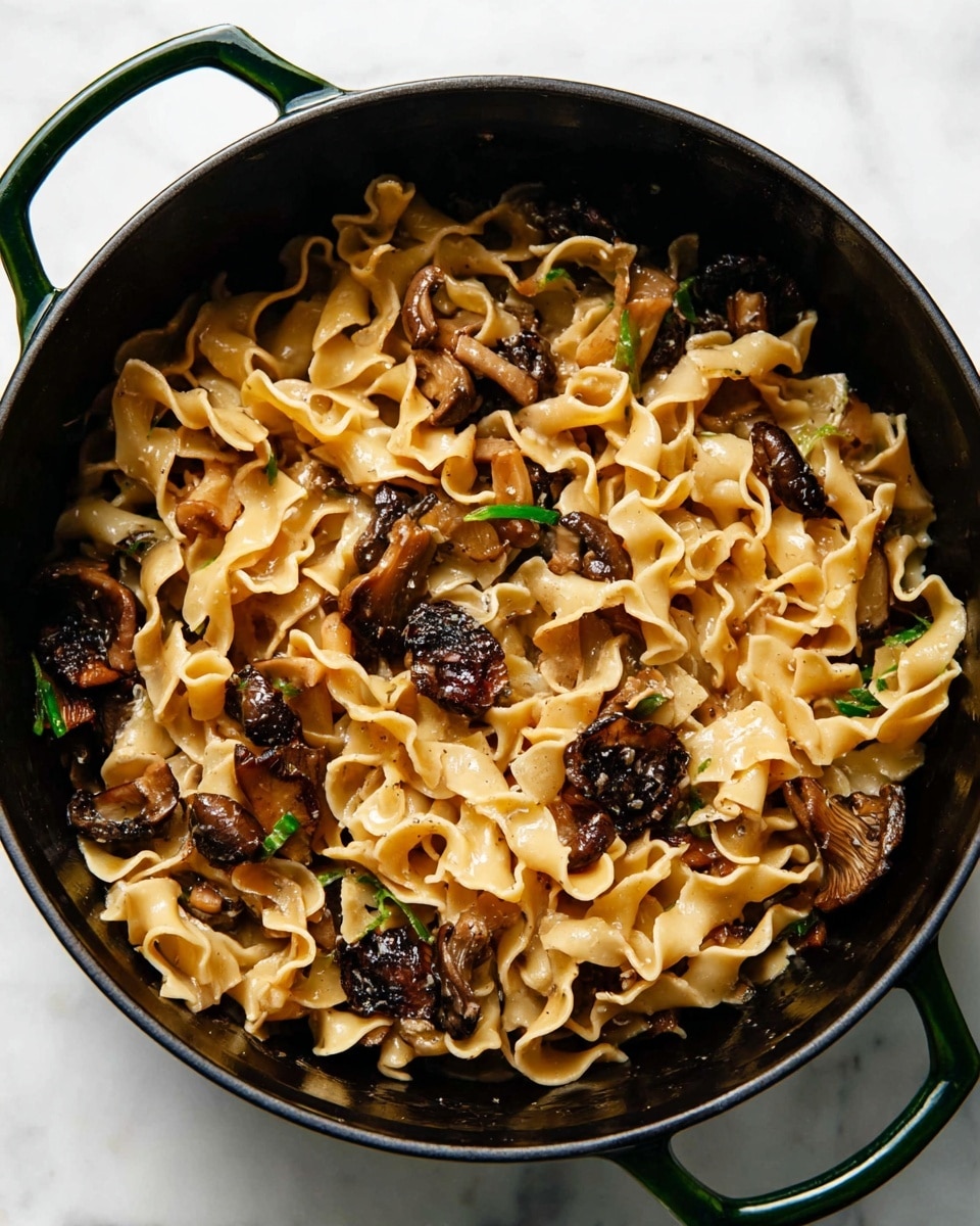 The image shows a black pot filled with wide, curly-edged pasta mixed with browned mushroom pieces. The pasta has a light golden-brown color with a smooth and slightly shiny texture, while the mushrooms are dark brown and slightly crispy. The pot has a small glimpse of a green handle on the side and is placed on a white marbled surface. photo taken with an iphone --ar 4:5 --v 7