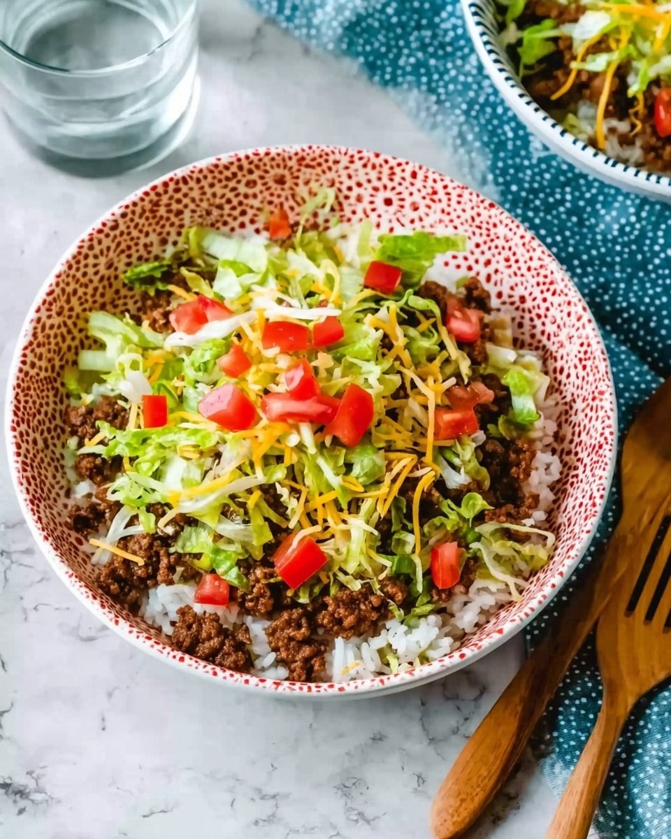 A white bowl with a red dotted pattern holds a layered taco salad. The bottom layer is plain white rice, topped with crumbled cooked ground beef, followed by shredded green lettuce and finely shredded yellow cheese. On top, there are small diced red tomatoes scattered over the salad. The bowl is placed on a white marbled surface, with a wooden fork and spoon on the right side. In the upper corner, there is a glimpse of another white bowl with a blue dotted pattern holding a similar dish, and a glass of water nearby. Photo taken with an iphone --ar 4:5 --v 7