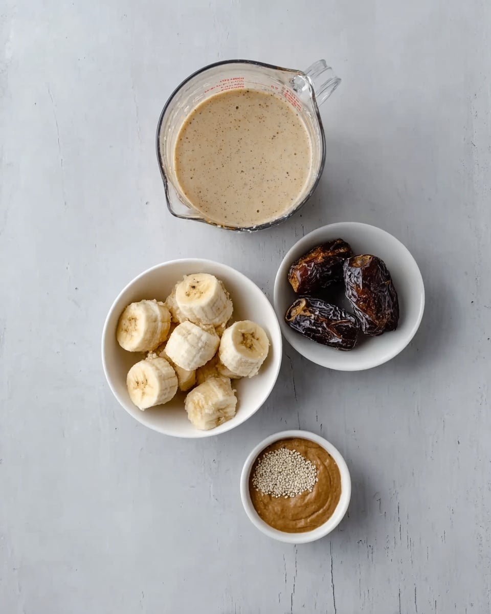 The image shows four white bowls arranged on a white marbled surface from top to bottom in a vertical line. The top bowl holds a large clear measuring cup filled with a beige liquid. Below it is a white bowl with several pieces of peeled and sliced bananas and three dates. The third smaller bowl contains a dark brown powder sprinkled with white grains on top. The last white bowl at the bottom has a smooth light brown paste. The overall view is clean and simple, highlighting the ingredients. Photo taken with an iphone --ar 4:5 --v 7