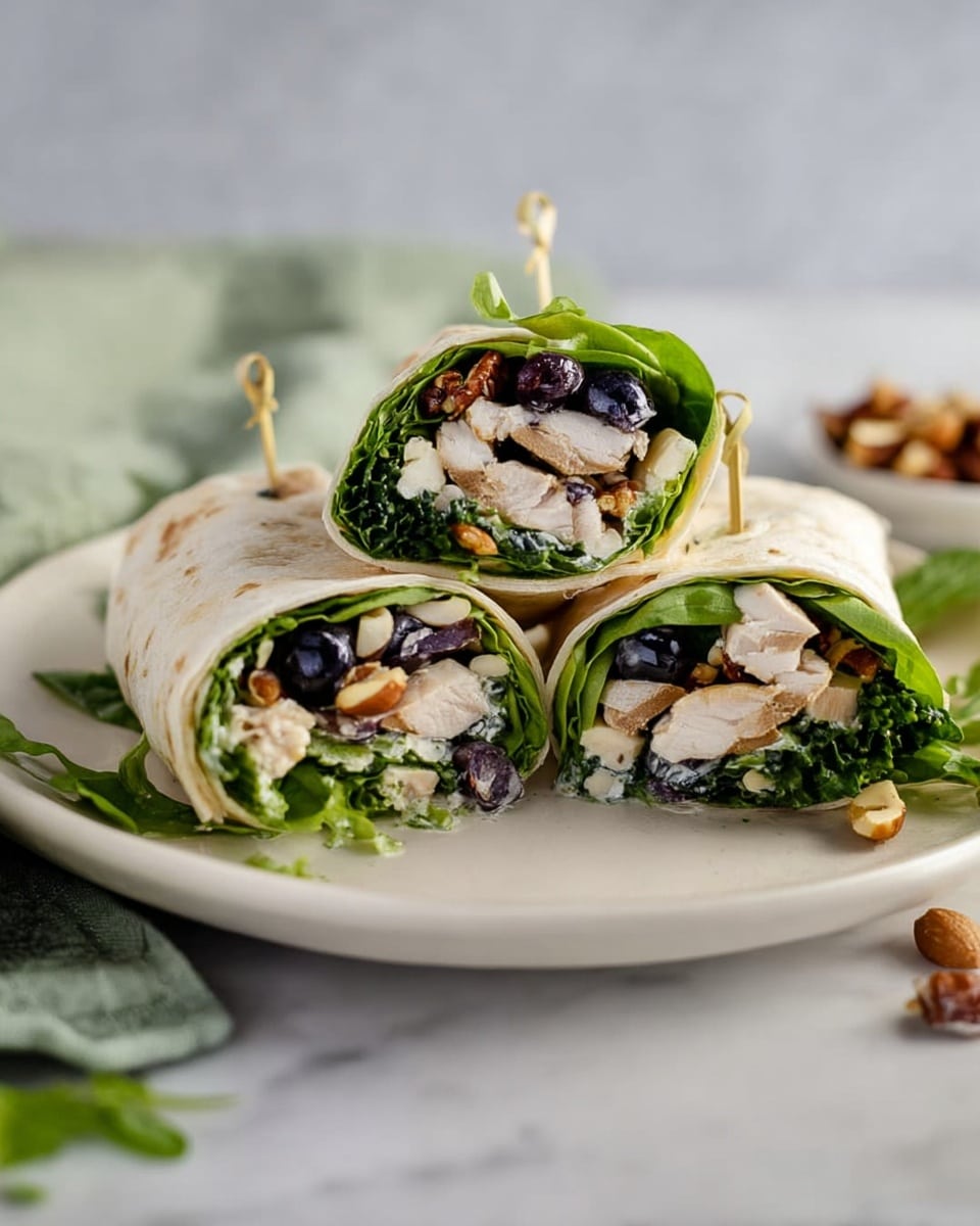 Three wraps cut in half are arranged on a white plate, each held together with a toothpick. The wraps show layers of green leafy lettuce on top, white chunks of cooked chicken below, scattered dark blue blueberries, and light brown nuts mixed in. The wraps are light beige with a soft texture. The plate sits on a white marbled surface with some greens and nuts loosely scattered around. Photo taken with an iphone --ar 4:5 --v 7