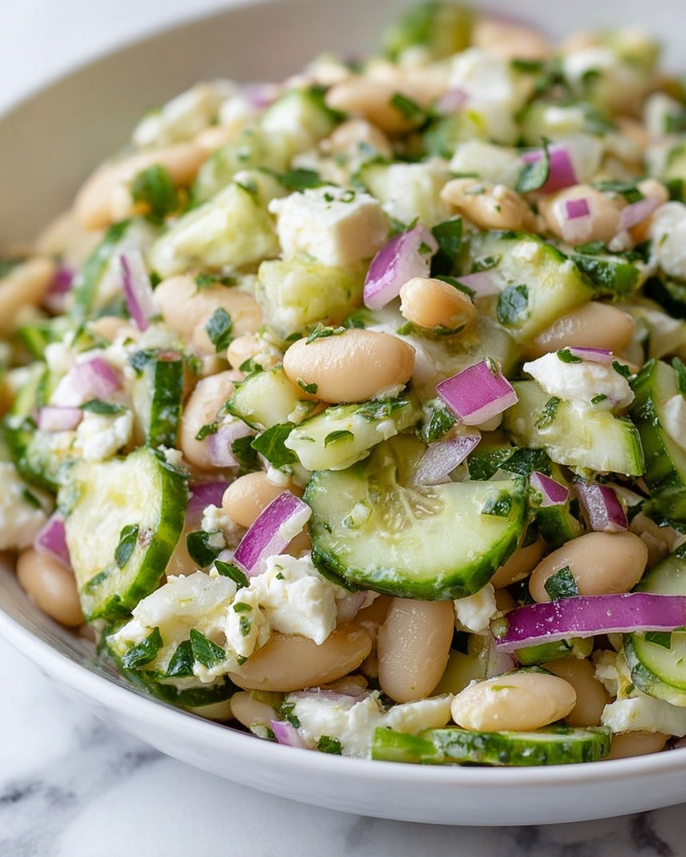 The image shows a close-up of a white bowl filled with a fresh salad made of white beans, sliced light green cucumbers, chopped purple onions, small pieces of white cheese, and green herbs mixed throughout. The salad layers are uneven and mixed, with the white beans and cheese chunks standing out against the soft green cucumber slices and bright purple onions. The salad looks moist with a light dressing, and the background is a white marbled surface. Photo taken with an iphone --ar 4:5 --v 7