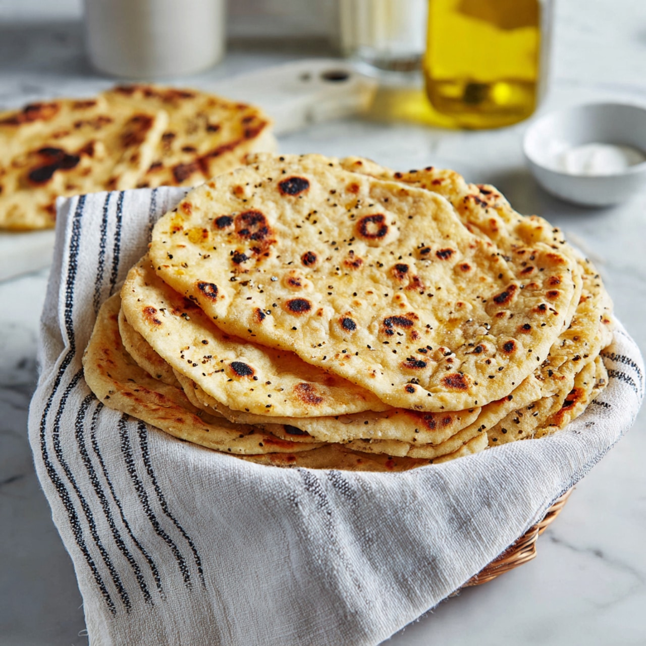 A round, light cream-colored flatbread with small golden-brown spots is cooking in a black cast iron skillet. The flatbread is puffy and slightly uneven in thickness, showing a soft and fresh texture. The skillet sits on a white marbled surface with some light shadows creating a natural look. Photo taken with an iphone --ar 4:5 --v 7