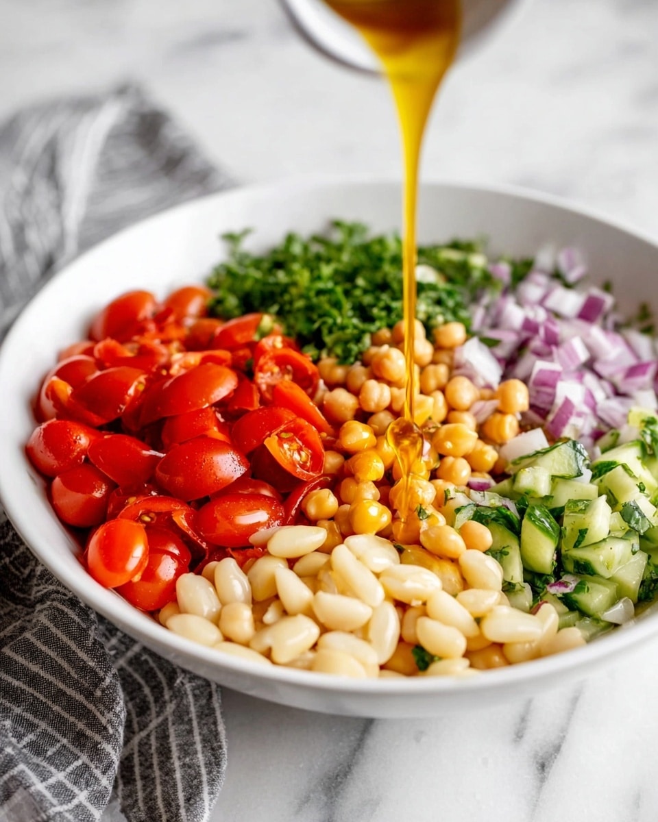 A white bowl filled with several colorful layers of chopped ingredients arranged separately in sections: bright red chopped cherry tomatoes on the left, creamy white large beans in the bottom right, light brown chickpeas in the upper center, finely chopped red onions in the top right, fresh green chopped parsley and cucumbers in the top right near the beans. A golden-colored liquid is being poured from above onto the beans. The bowl is placed on a white marbled surface with a gray and white striped cloth nearby. photo taken with an iphone --ar 4:5 --v 7