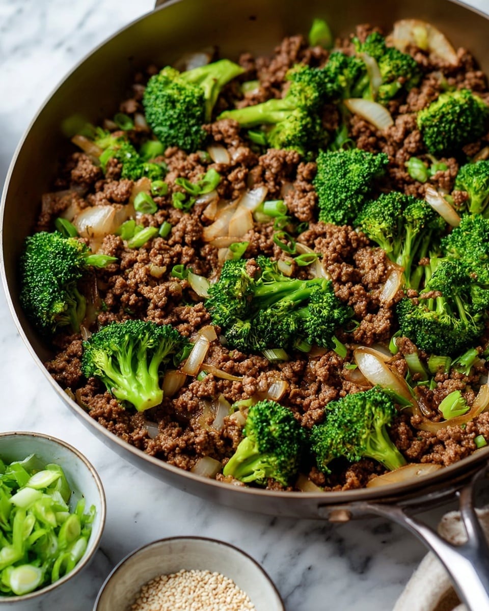 A close-up view of a frying pan with cooked ground meat mixed with sautéed onions and bright green broccoli florets. The meat forms a textured brown layer throughout, with chunks of soft, slightly translucent onions scattered evenly. The broccoli pieces have vibrant green tops with thicker, lighter green stems, sitting on and partially mixed into the meat and onions. The pan handle is visible at the bottom center, resting on a white marbled surface. Small bowls with green onion slices and white sesame seeds are blurred in the foreground. Photo taken with an iphone --ar 4:5 --v 7