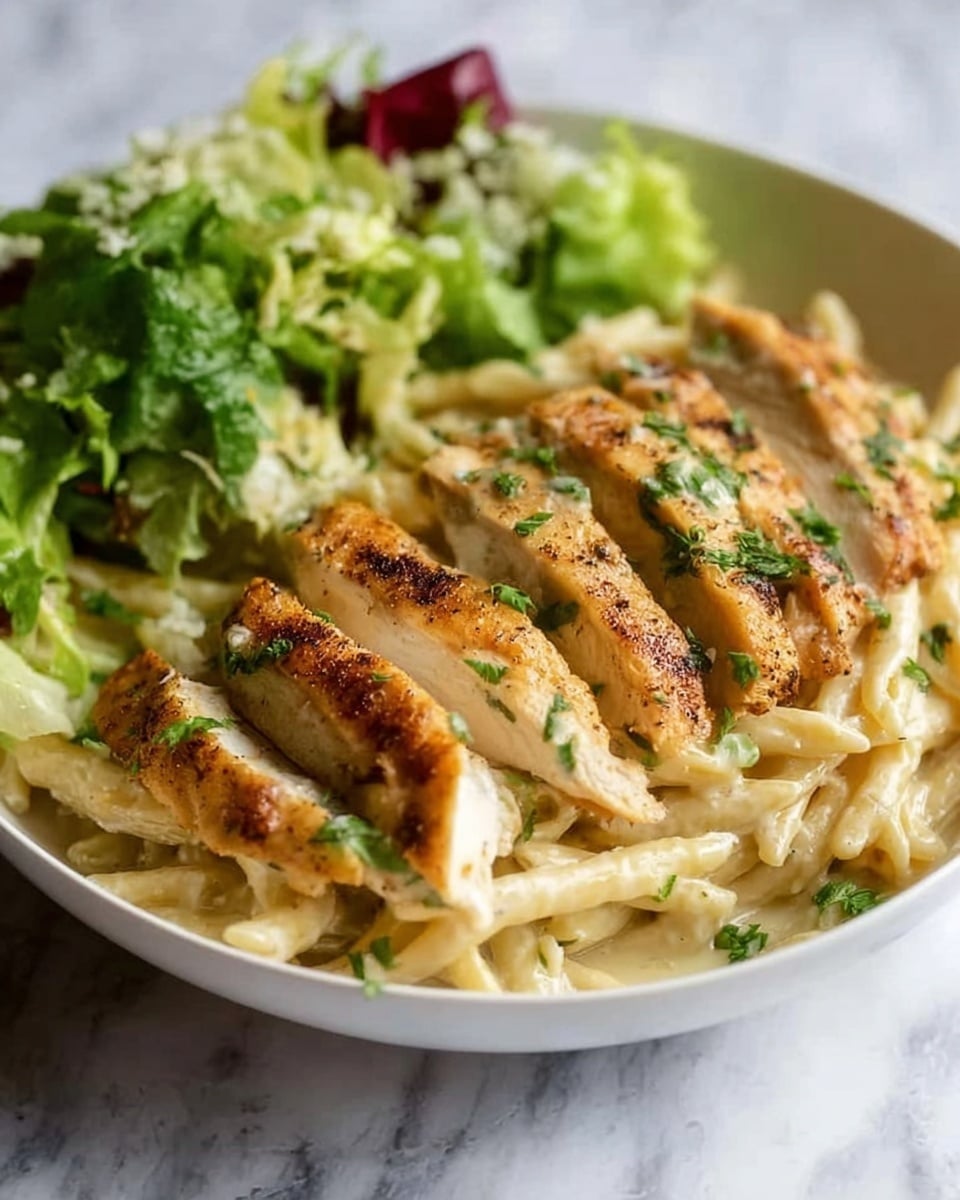 The image shows a white bowl filled with creamy pasta topped with several slices of golden-brown grilled chicken. The chicken slices are placed on top, with a slightly crispy texture and sprinkled with chopped green herbs. Underneath, the pasta is coated with a light cream sauce, giving it a smooth and shiny appearance. On one side of the bowl, there is a small fresh green salad that includes leafy lettuce and some red vegetable pieces. The bowl is set on a white marbled surface. Photo taken with an iphone --ar 4:5 --v 7