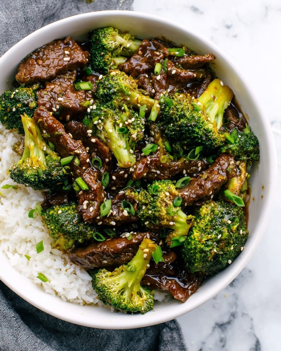 The image shows a white bowl with two main layers: on the bottom right is a layer of white rice, and on top covering most of the bowl are pieces of dark brown cooked beef mixed with bright green broccoli florets. The beef and broccoli are coated in a shiny dark sauce, giving a wet texture. Small white sesame seeds and chopped green onions are sprinkled on top, adding texture and color contrast. The bowl sits on a white marbled surface with a gray cloth partially visible on the bottom left side. photo taken with an iphone --ar 4:5 --v 7