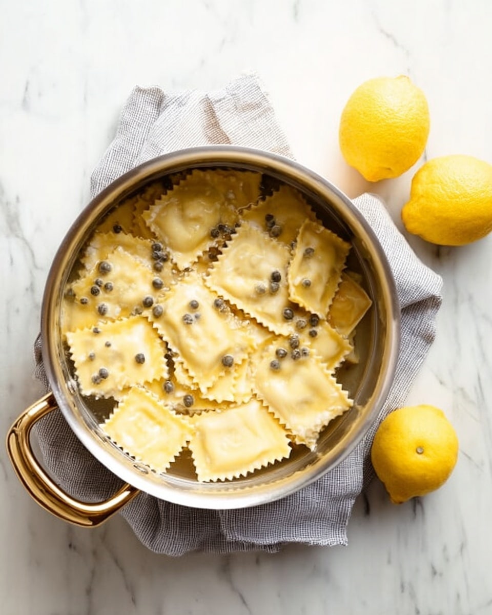 A stainless steel pot filled with square ravioli pasta floating in clear water, each ravioli having a soft pale yellow color with slightly crinkled edges and dark small green peppercorns spread evenly on top. The pot rests on a light grey cloth on a white marbled surface. To the right, two yellow lemons lie directly on the white marbled surface. Photo taken with an iphone --ar 4:5 --v 7