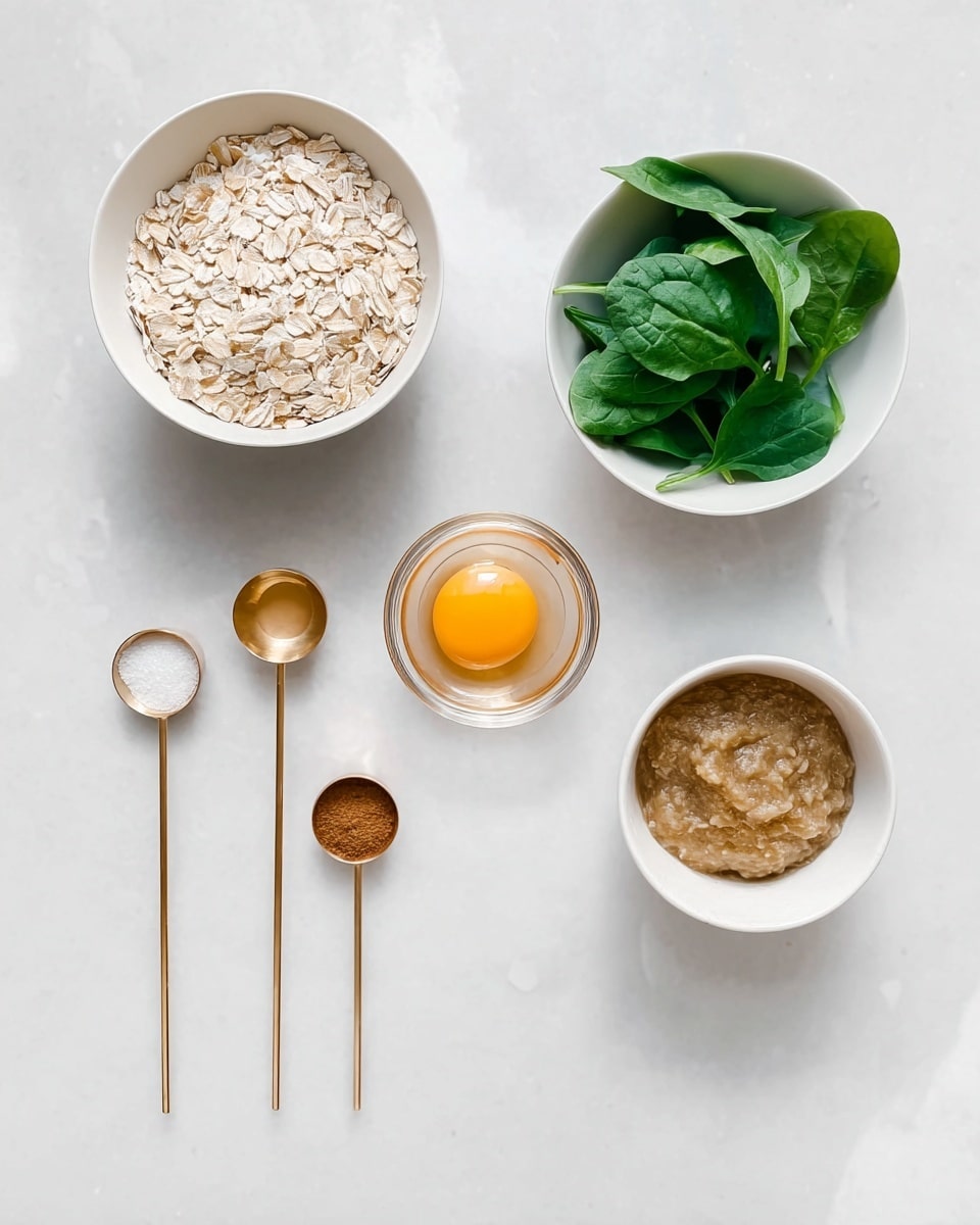 The image shows several small white bowls and gold measuring spoons arranged on a white marbled surface. There is one white bowl filled with light beige oats, another with fresh green spinach leaves, and a smaller bowl with a brownish puree. In the center, a clear small glass bowl holds an egg yolk with a smooth texture. To the left of the bowls, three gold measuring spoons contain white salt, brown cinnamon powder, and amber liquid honey, placed in a diagonal row. The overall arrangement is neat and clean, with soft natural lighting. photo taken with an iphone --ar 4:5 --v 7