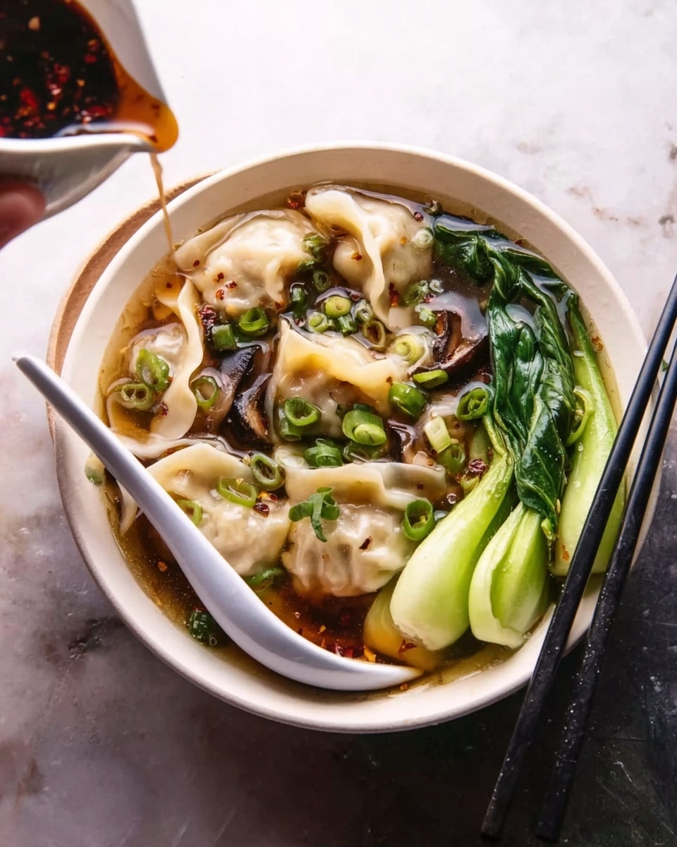 A white bowl filled with clear broth holding several plump dumplings with soft, beige wrappers floating on top. On one side, bright green steamed bok choy and dark, thick slices of mushroom lay partially submerged in the broth. Thinly sliced green onions are sprinkled over the dumplings adding small green spots. A white spoon rests inside the bowl at the front, and a pair of black chopsticks are placed diagonally across the bowl. A woman's hand holds a white pouring vessel tilted above the bowl, dripping a dark sauce with a chili-like texture over the dumplings. The setup is on a white marbled surface. photo taken with an iphone --ar 4:5 --v 7