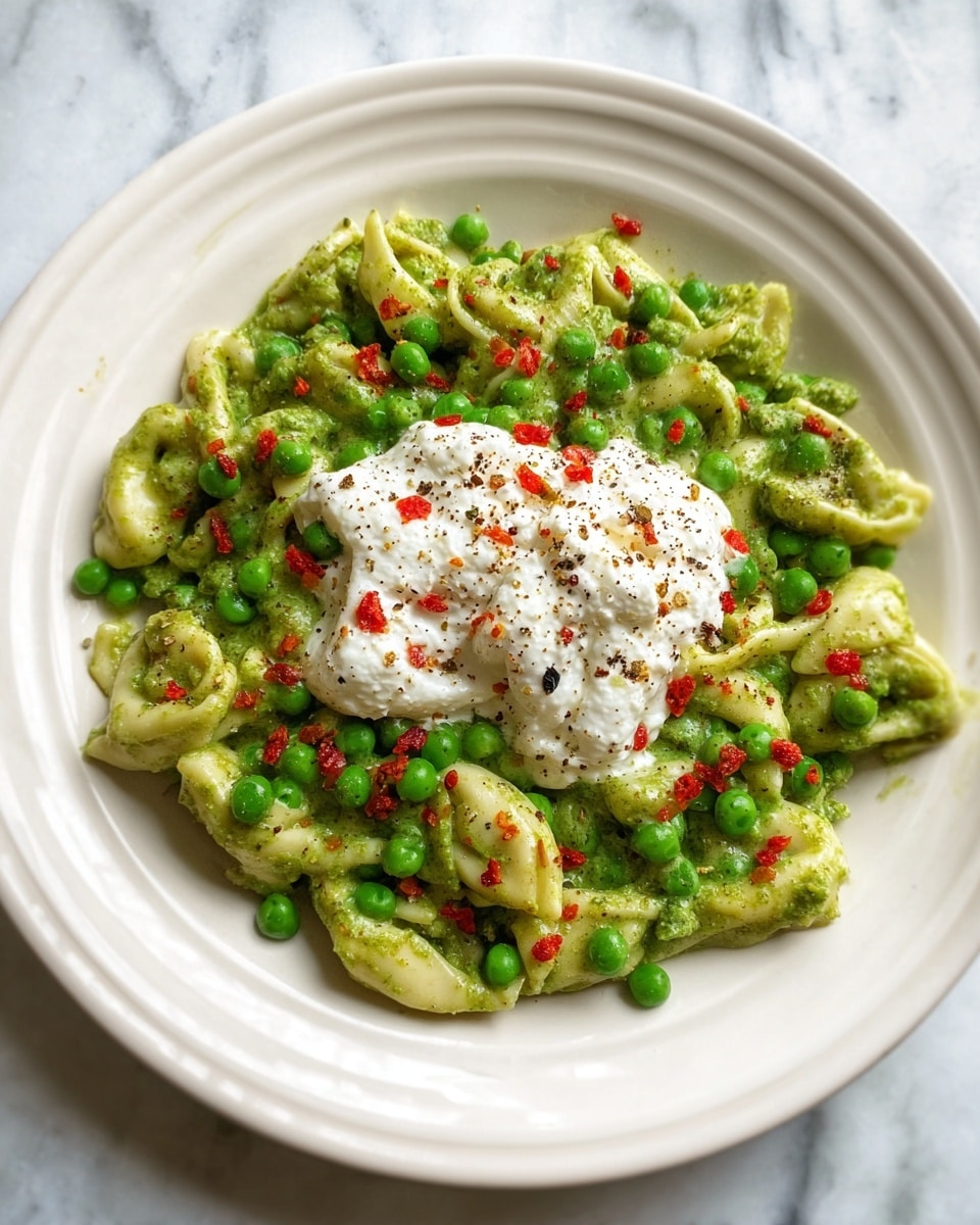 A white plate holds a dish with three main layers: the base layer is green tortellini pasta mixed evenly with bright green peas and small red pepper pieces scattered all over. On top of the pasta and peas is a dollop of white cottage cheese with a slightly lumpy texture, sprinkled with black pepper and red pepper bits. The plate is set on a white marbled surface. photo taken with an iphone --ar 4:5 --v 7