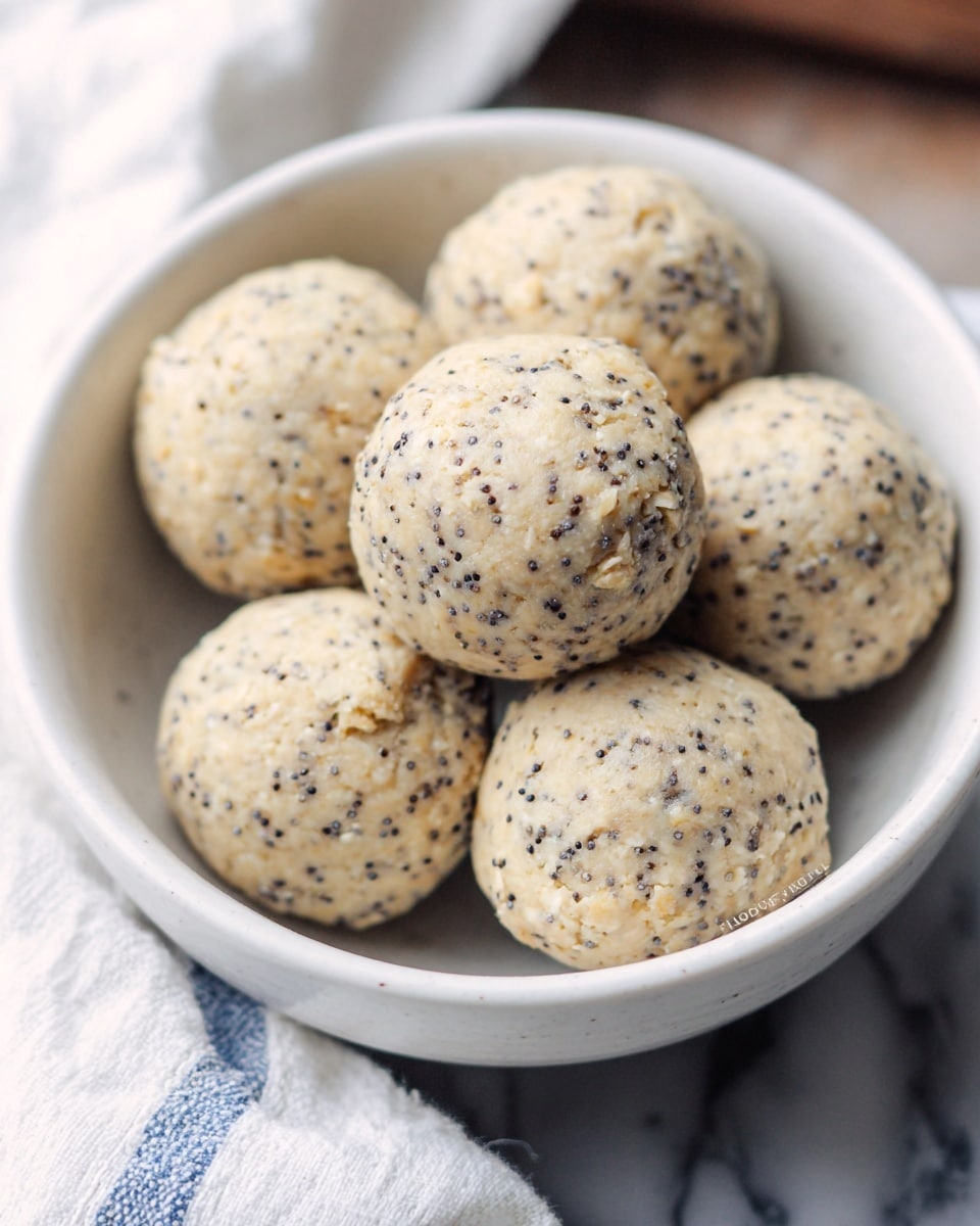 A close-up image shows a white bowl filled with six round, light-colored dough balls speckled with small black seeds. The dough balls have a slightly rough texture with visible oats mixed in, giving them a natural, homemade look. The bowl sits on a white marbled surface partially covered by a white and blue cloth. The overall feel is bright and clean, focusing on the textured, lightly colored dough balls stacked closely together inside the bowl photo taken with an iphone --ar 4:5 --v 7
