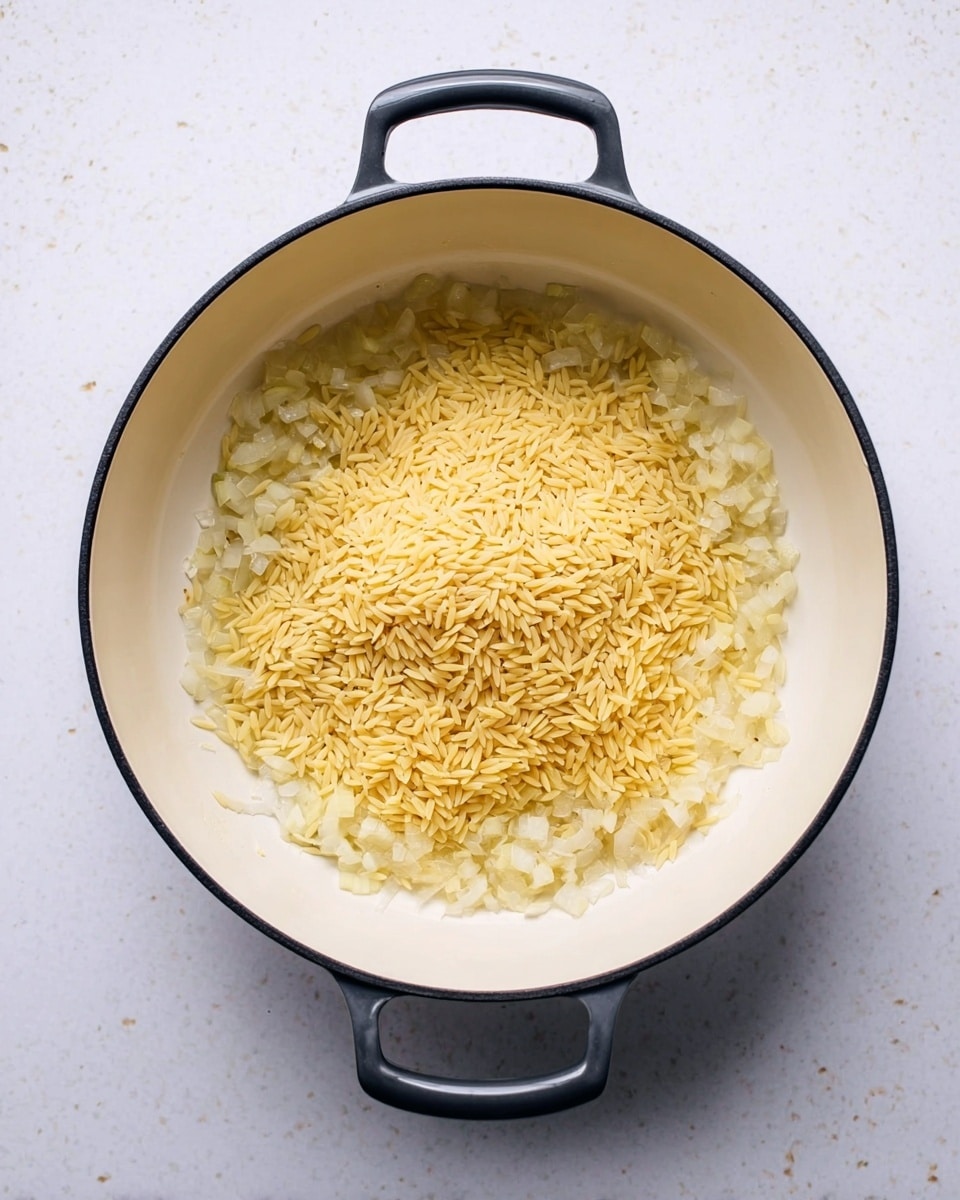 A white pan with black edges and dark handles is placed on a white marbled surface. Inside the pan, there is a layer of chopped onions frying in oil, showing translucent and shiny textures around the edges. In the center, on top of the onions, is a pile of dry orzo pasta, which is small, smooth, and golden yellow in color, creating a contrast with the lighter onions beneath. The scene is bright and clear, with the ingredients ready to be cooked further. Photo taken with an iphone --ar 4:5 --v 7