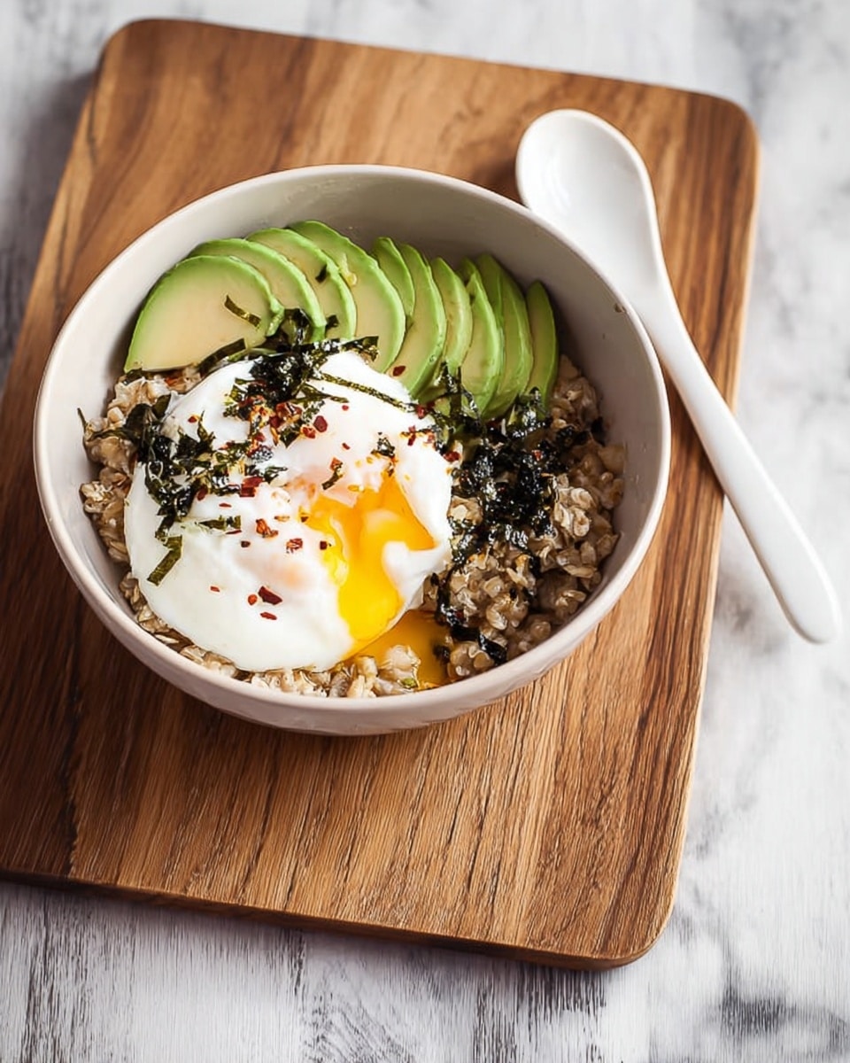 A white bowl filled with three main layers sits on a wooden board over a white marbled surface. The bottom layer is a bed of brown rolled oats with a rough, grainy texture. On top of this, there is a neat row of light green avocado slices, smooth and creamy in appearance, placed on one side of the bowl. Next to the avocado is a bright white poached egg with a soft, fluffy texture, topped with a shiny, golden-yellow runny yolk that is slightly broken. The egg is sprinkled with small bits of dark green seaweed and tiny red chili flakes scattered lightly around. A white spoon lies beside the bowl on the wooden board. Photo taken with an iphone --ar 4:5 --v 7