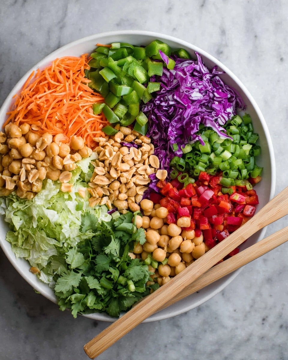 A white bowl filled with seven colorful layers of ingredients arranged separately in sections. Starting from the top left going clockwise: shredded orange carrots, diced green bell peppers, shredded purple cabbage, chopped green lettuce, light beige chickpeas, diced red bell peppers, and chopped green onions with some fresh cilantro leaves next to them. In the center, a small pile of roasted peanuts adds texture and light brown color. A pair of light wooden salad spoons rest on the right edge of the bowl. The bowl sits on a white marbled surface. photo taken with an iphone --ar 4:5 --v 7