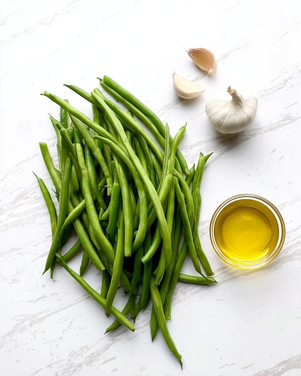 The image shows fresh green beans in a loose pile on a white marbled surface. To the right of the beans, there is a small clear container filled with golden yellow oil. Above the oil are two cloves of garlic with white and slightly tan skin. The background is clean and bright with a white marbled texture. photo taken with an iphone --ar 4:5 --v 7