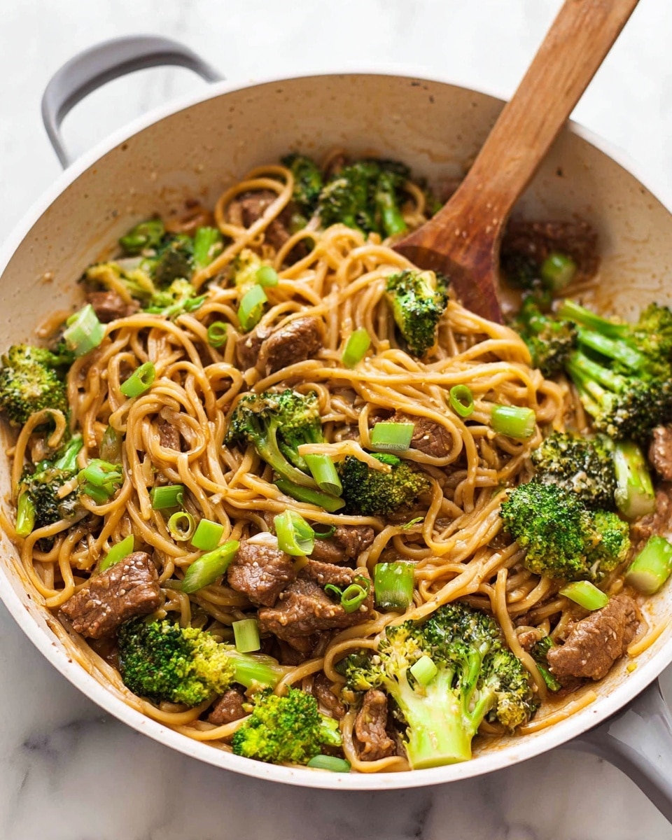 The image shows a white frying pan filled with a colorful stir-fry dish. Inside, there are thick, light brown noodles intertwined with green broccoli florets and green onion slices sprinkled on top. There are also pieces of cooked brown meat mixed evenly throughout the dish. The stir-fry is slightly glossy, indicating a light sauce coating. Two wooden cooking spoons rest inside the pan, one positioned on the left side and the other on the right, partially submerged in the food. The pan is placed on a white marbled surface. photo taken with an iphone --ar 4:5 --v 7