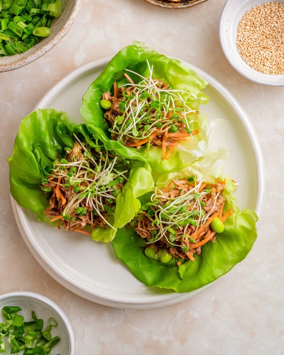 The image shows three lettuce cups on a white plate, each cup made from large bright green leaves wrapping layers of shredded light brown cooked meat, thin orange carrot strips, small pale green edamame beans, and a mix of green sprouts on top. The plate sits on a white marbled surface with small white bowls nearby, one filled with green chopped scallions and another bowl with light brown sesame seeds, all creating a fresh and colorful arrangement. Photo taken with an iphone --ar 4:5 --v 7