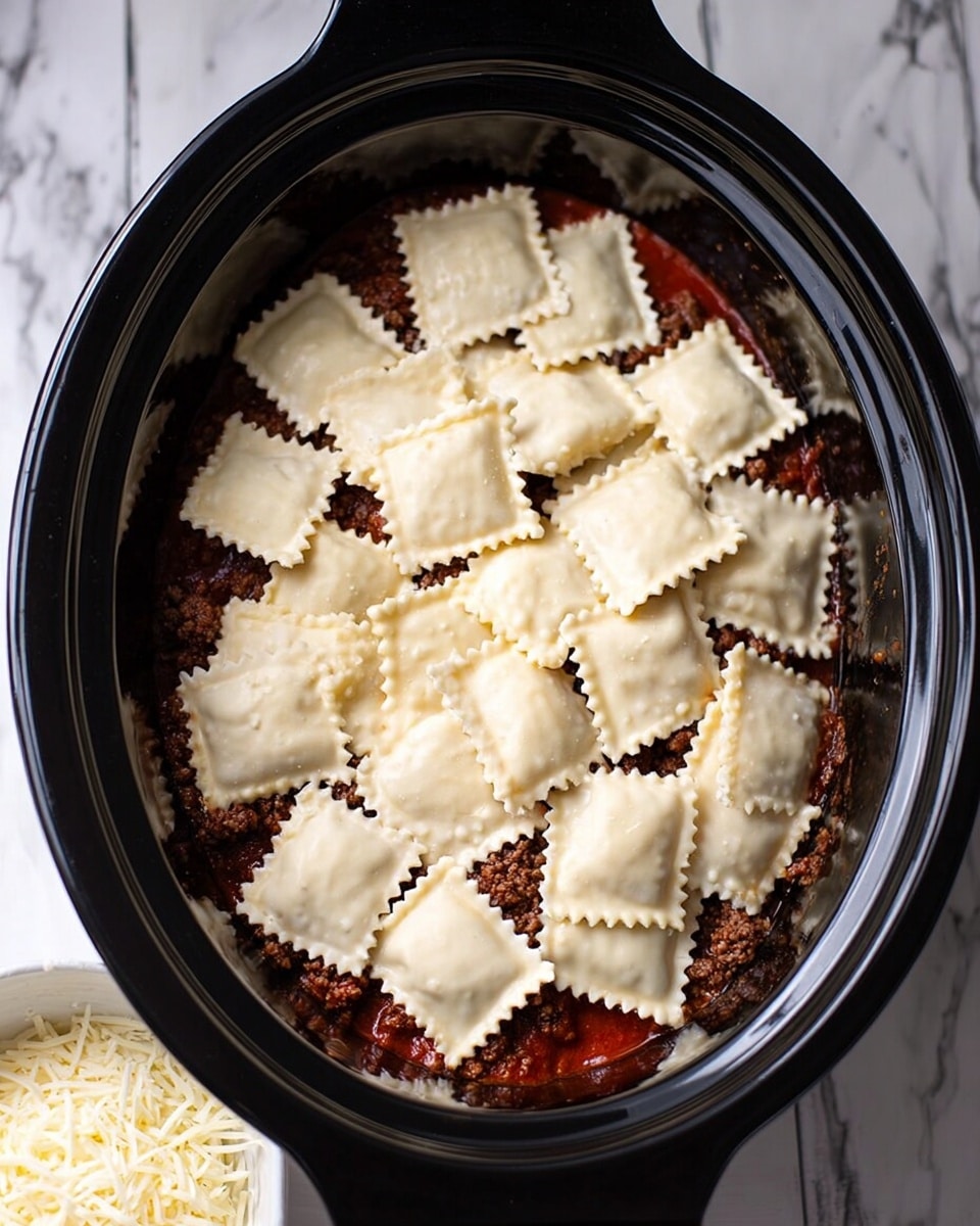 The image shows a black oval slow cooker filled with layers of food, starting with a bottom layer of red sauce, followed by a layer of cooked ground meat, and topped with a single layer of square-shaped ravioli with crimped edges, arranged closely together to cover the whole surface. In the bottom left corner, part of a white bowl filled with shredded white cheese is visible. The slow cooker is placed on a white marbled surface. photo taken with an iphone --ar 4:5 --v 7