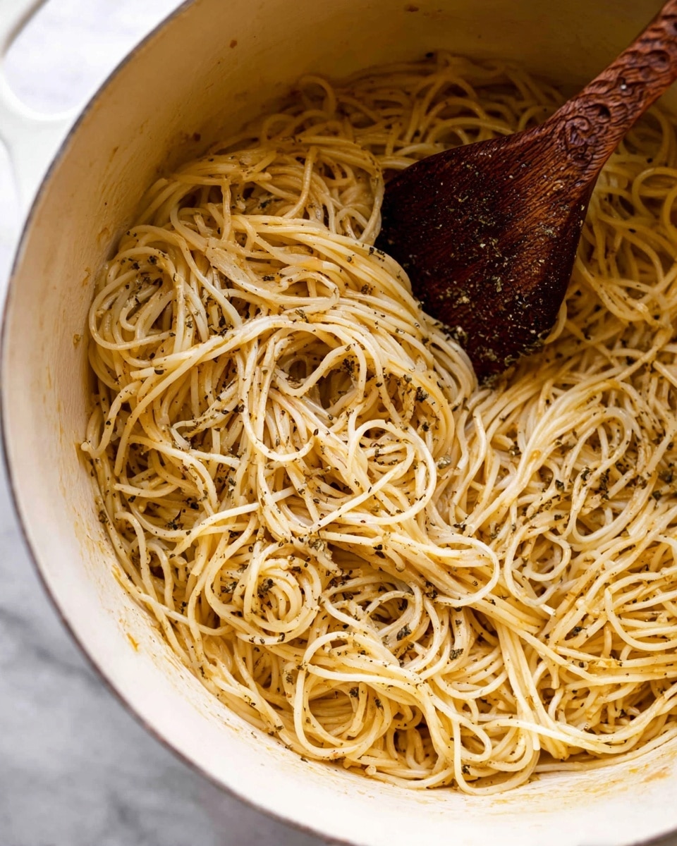 A large white bowl sits on a white marbled surface, filled with thin yellow spaghetti noodles tossed loosely throughout. The noodles are lightly coated in oil or butter, giving them a slight shine, and are sprinkled with small bits of green herbs and a dusting of grated white cheese. A silver fork with a textured handle rests on the right side inside the bowl, partially twined with noodles. There are small bits of black pepper evenly scattered across the pasta, adding texture and color. In the background, a round wooden bowl with green herbs is partly visible along with a block of hard yellow cheese, enhancing the fresh and simple look. Photo taken with an iphone --ar 4:5 --v 7