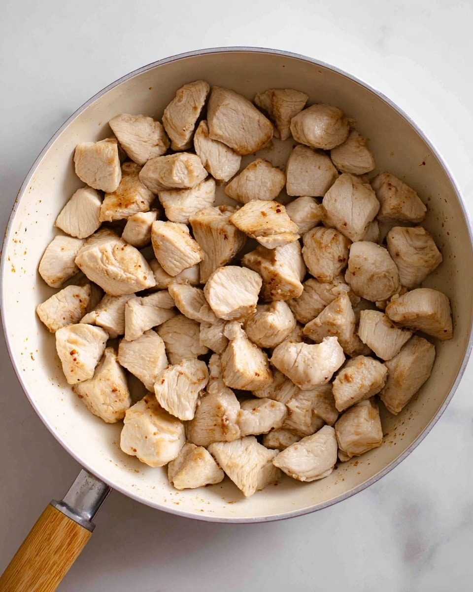 A white pan with a wooden handle filled with many pieces of cooked chicken chunks. The chicken pieces are light beige with slight brown grill marks and look tender. The pan sits on a white marbled surface. photo taken with an iphone --ar 4:5 --v 7