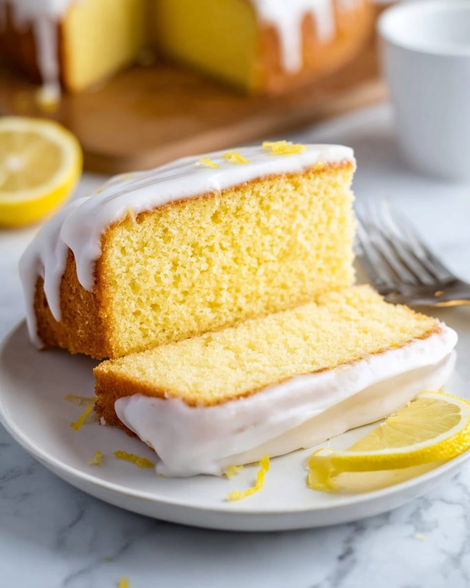 Two slices of yellow lemon cake with a thick white icing layer on top and sides are stacked on a white plate. The bottom slice lies flat, while the top slice is placed diagonally across it. Two lemon wedges and a silver fork rest behind the slices on the plate. The scene is set on a white marbled surface with part of a wooden board and a whole lemon blurred in the background. Photo taken with an iphone --ar 4:5 --v 7