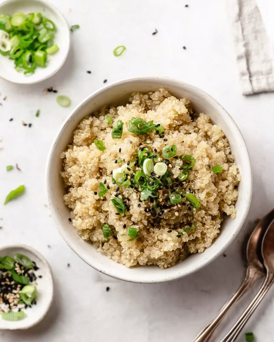 A white bowl sits on a white marbled surface, filled with three layers of fluffy cooked quinoa that is light beige in color and shows the tiny round grains clearly. The top layer of quinoa is garnished with small green scallion slices, finely chopped herbs, and scattered black sesame seeds, adding splashes of dark and fresh green tones. Around the bowl, there are small white dishes with more chopped green onions and herbs, along with a couple of silver spoons placed casually nearby. The overall look is fresh and simple, with soft natural lighting highlighting the textures. photo taken with an iphone --ar 4:5 --v 7