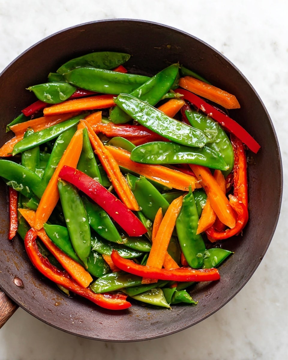 The image shows a dark pan filled with brightly colored vegetables. There are green snap peas scattered all over, shiny and fresh with a smooth texture. Mixed with them are bright orange carrot slices, some showing slight browning from cooking. Also, long red bell pepper strips lie among the vegetables, adding a vibrant contrast. The pan is placed on a white marbled surface that adds a clean, simple background to the colorful mix. photo taken with an iphone --ar 4:5 --v 7