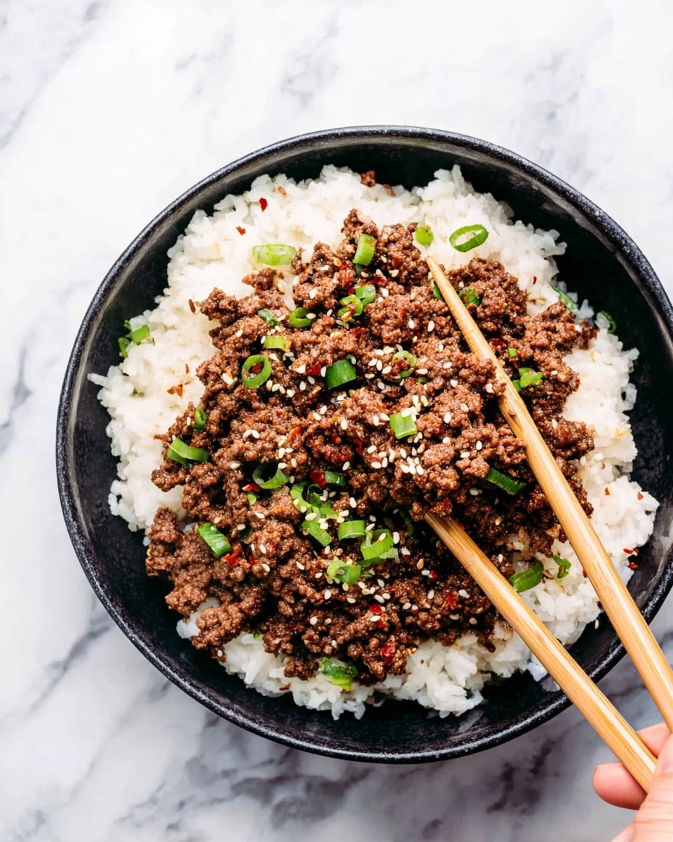 A round black bowl filled with two layers; the bottom layer is white rice with a soft, fluffy texture, and the top layer is cooked ground meat, brown and crumbly. The meat is scattered with small green chopped scallions and sprinkled with white sesame seeds and tiny red chili flakes. A pair of light brown chopsticks is placed inside the bowl, held by a woman's hand, lifting some of the meat. The bowl is set on a white marbled surface. photo taken with an iphone --ar 4:5 --v 7