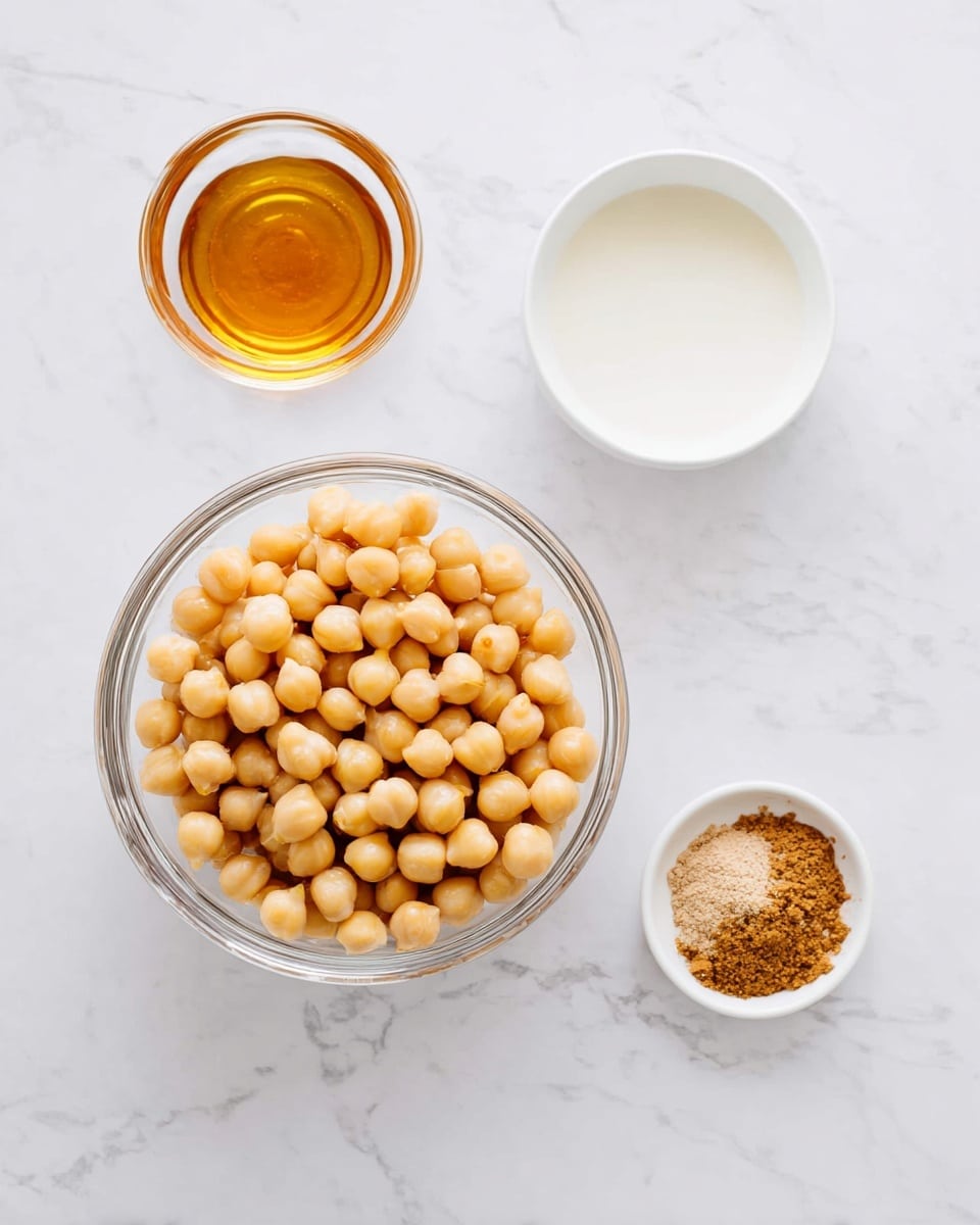 The image shows a round clear glass bowl filled with light beige chickpeas in the center placed on a white marbled surface. Around the bowl, there are three small white bowls spaced evenly: the top right bowl contains a smooth white liquid, the bottom right bowl holds a small pile of light brown powder, and the left bowl has a golden amber-colored syrup. The composition is simple with all items displayed neatly and cleanly. Photo taken with an iphone --ar 4:5 --v 7