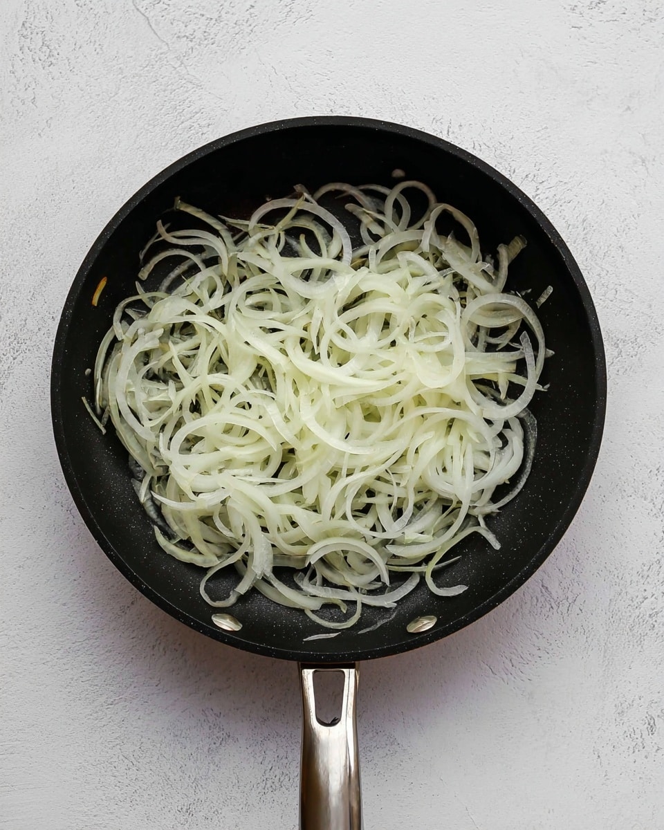 A black frying pan with two metal handles holds a single layer of thinly sliced white onions, spread evenly to cover the pan's surface. The onions have a pale translucent color with a slight shine, showing their fresh and raw state. The pan rests on a white marbled textured surface, creating a clean, simple background. photo taken with an iphone --ar 4:5 --v 7
