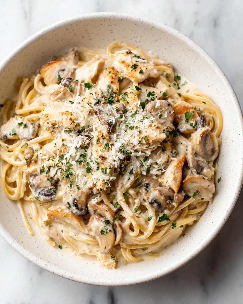 A white textured bowl holds creamy pasta with three main layers: the base layer of long spaghetti noodles tangled together in light beige, topped with a smooth white cream sauce that covers the noodles evenly, scattered with light brown cooked mushroom slices with some dark gills showing, and pieces of light golden cooked chicken. The top layer is sprinkled with finely grated white cheese and small green chopped herbs, adding color and texture. The bowl sits on a white marbled surface. photo taken with an iphone --ar 4:5 --v 7