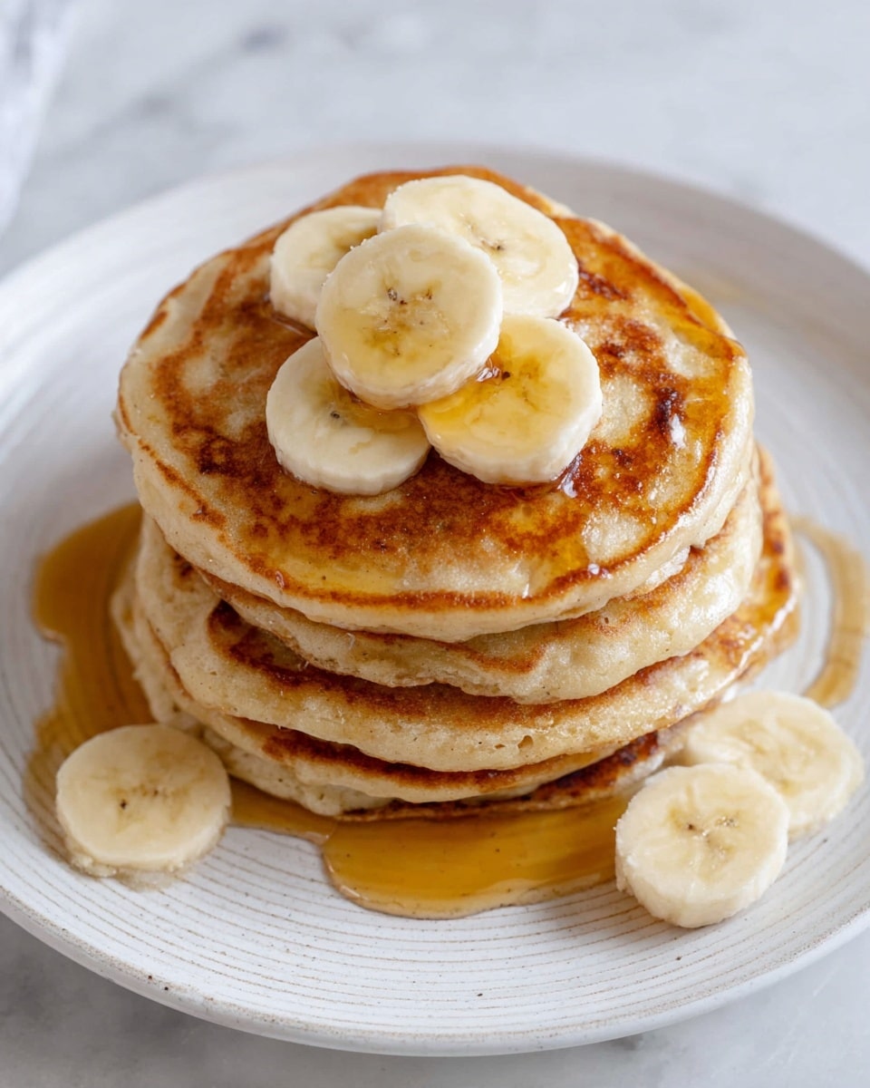 A stack of six golden brown pancakes sits in the center of a white plate with a subtle textured edge. The pancakes have a soft, fluffy texture with slight browning spots and are layered neatly. On top, three slices of banana are placed in a small cluster, showing pale yellow color and soft texture. More banana slices rest on the plate beside the stack. Amber syrup glistens, flowing slowly over the top pancake and pooling gently around the base, adding a shiny and sticky surface. The whole scene is set on a white marbled surface. photo taken with an iphone --ar 4:5 --v 7