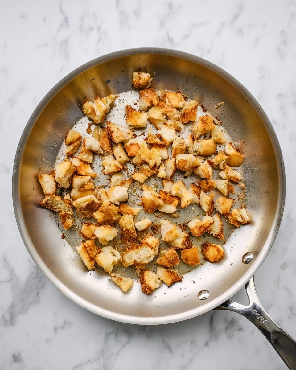 A top view of a silver frying pan placed on a white marbled surface, filled with scattered small pieces of golden brown fried food that appear crispy and uneven in shape, with some lightly browned edges and a slightly oily texture, showing a mix of light and darker golden colors across the pieces. photo taken with an iphone --ar 4:5 --v 7