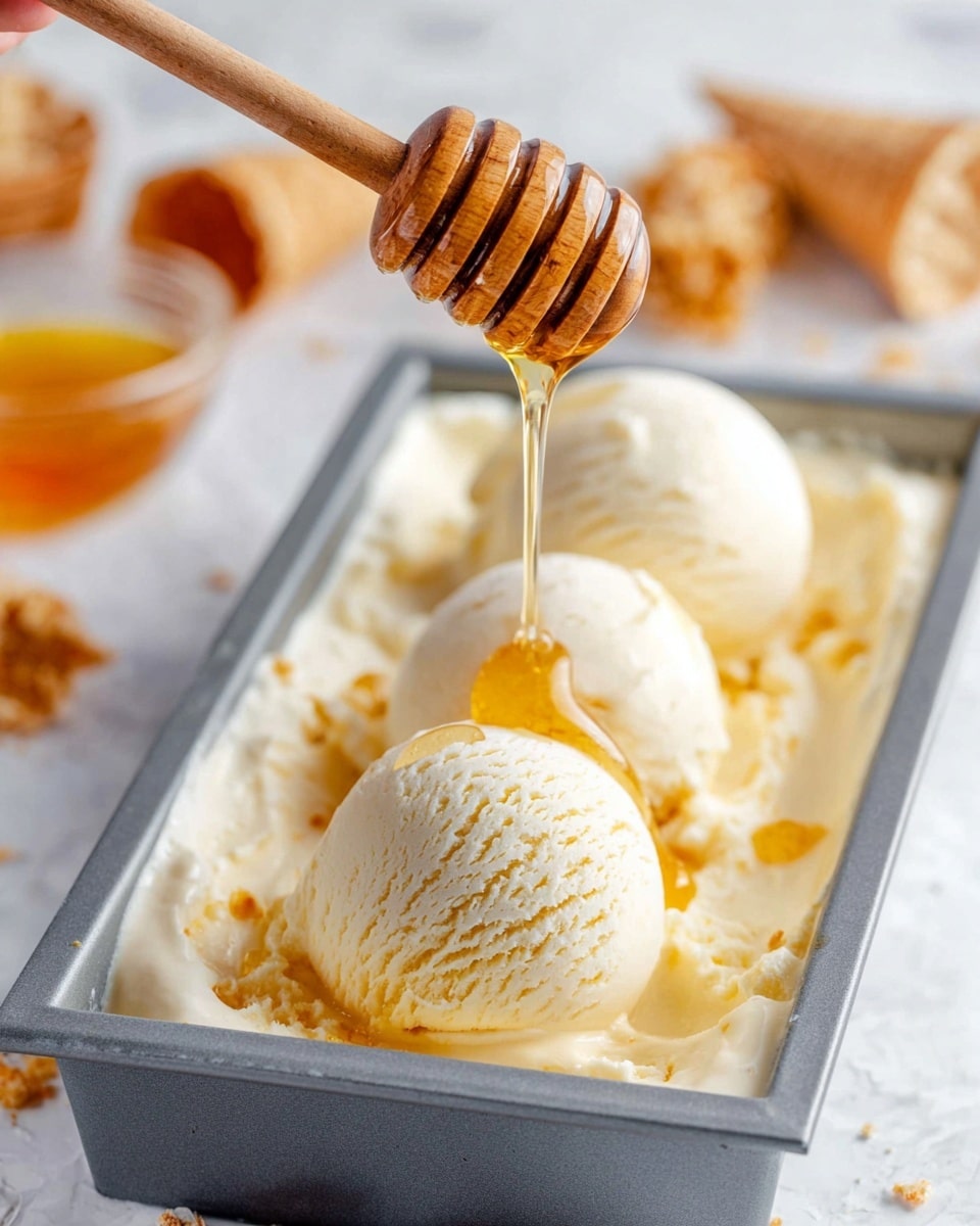 The image shows three large scoops of creamy, pale yellow ice cream arranged inside a rectangular container with a gray rim, placed on a white marbled surface. A woman's hand holds a wooden honey dipper above the center scoop, and golden honey drips in a smooth stream, spreading shiny lines over the soft, smooth ice cream. In the blurred background, there are some waffle cone pieces and a small dish filled with honey, adding warm orange and brown tones, creating a cozy and sweet atmosphere. photo taken with an iphone --ar 4:5 --v 7