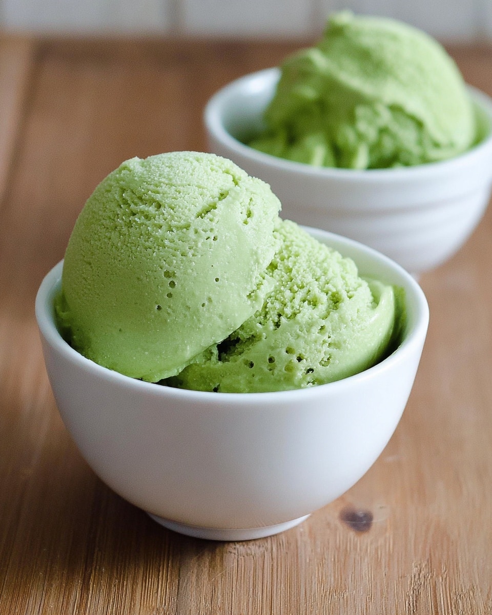 Two white cups filled with bright green ice cream, each showing a single scoop with a smooth but slightly textured surface. The front cup is in clear focus, revealing small air pockets and a creamy texture, while the back cup is blurred but still shows the same vibrant green color. Both cups sit on a light brown wooden surface. Photo taken with an iphone --ar 4:5 --v 7