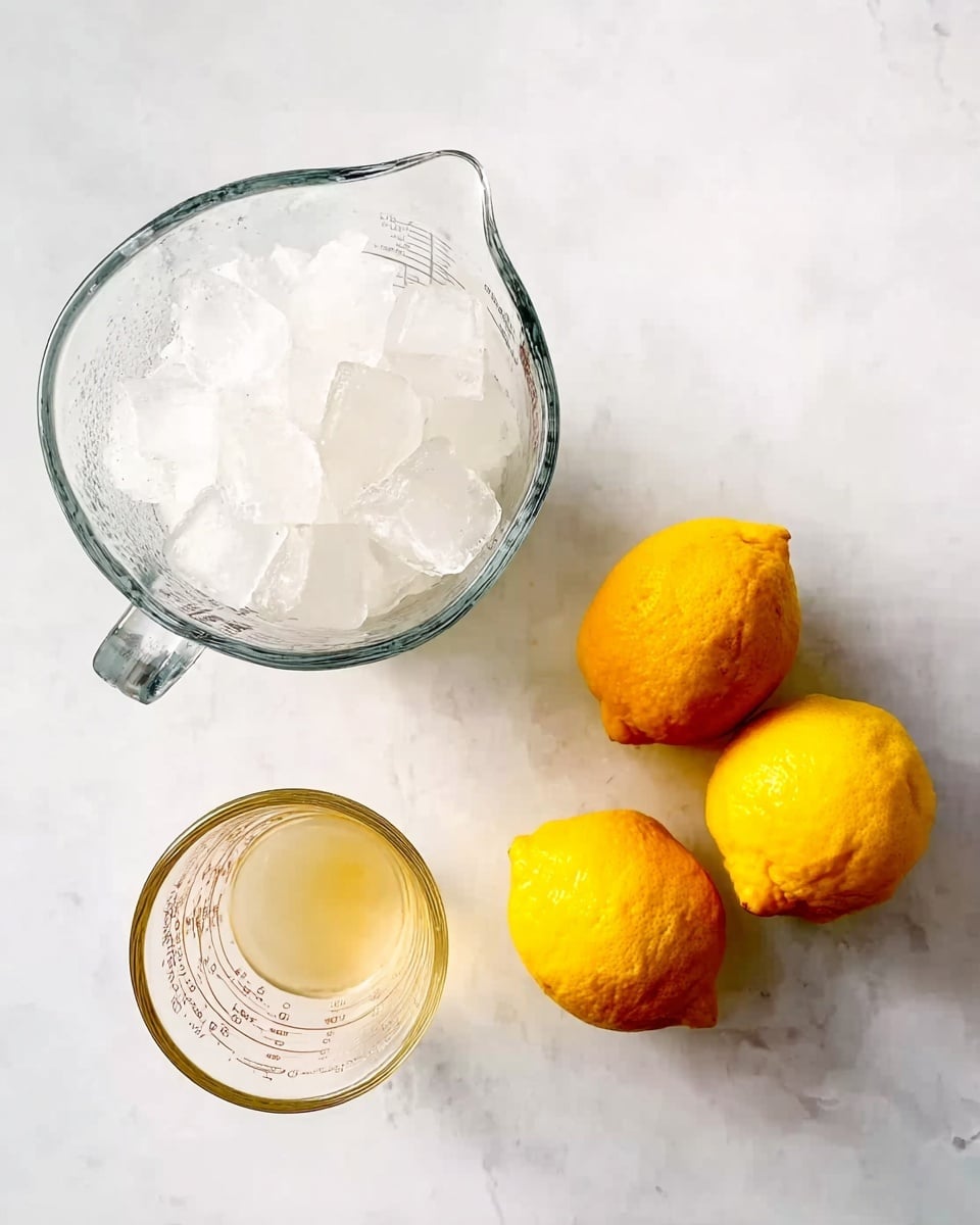 A clear glass measuring jug filled with white ice cubes sits on the top left of a white marbled surface, while three bright yellow lemons with slightly rough skin are placed together on the right side. Below the ice jug, there is a smaller clear glass measuring jug containing a pale straw-colored liquid. The scene shows simple ingredients laid out on a clean white marbled background. photo taken with an iphone --ar 4:5 --v 7