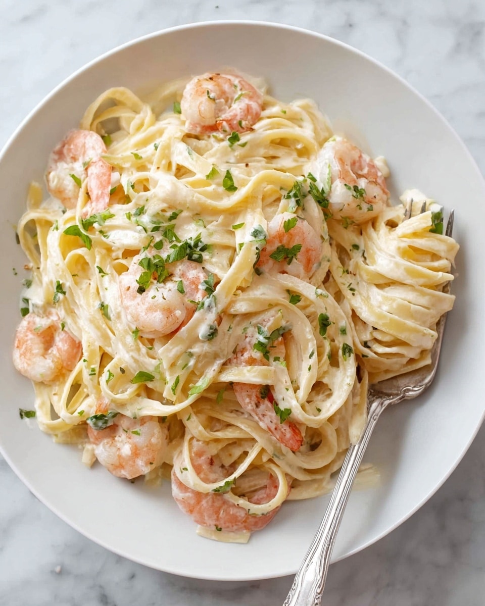 A white plate filled with creamy fettuccine pasta with shrimp, the pasta looking smooth and coated in a light white sauce. There are several cooked shrimp with a light pink color spread evenly through the noodles. Small green herbs, likely parsley, are sprinkled on top, adding a fresh touch. A silver fork rests on the right side of the plate, twirling some of the pasta, all set on a white marbled surface. photo taken with an iphone --ar 4:5 --v 7