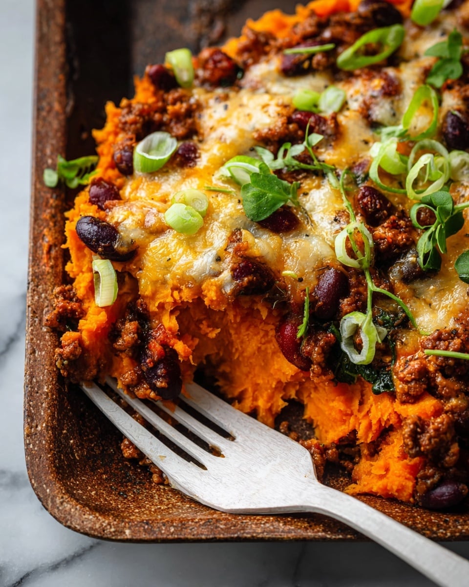 This dish is served in a close-up view in a baking tray, showing two layers. The bottom layer is bright orange mashed sweet potatoes with a soft, smooth texture. On top is a thick layer of cooked ground meat mixed with dark red kidney beans and bits of dark leafy greens, covered by a golden, melted cheese layer with a bubbly texture. Thin green onion slices and fresh small green leaves are sprinkled over for color. A white fork is placed under the food on the right side. The background is a white marbled texture. photo taken with an iphone --ar 4:5 --v 7
