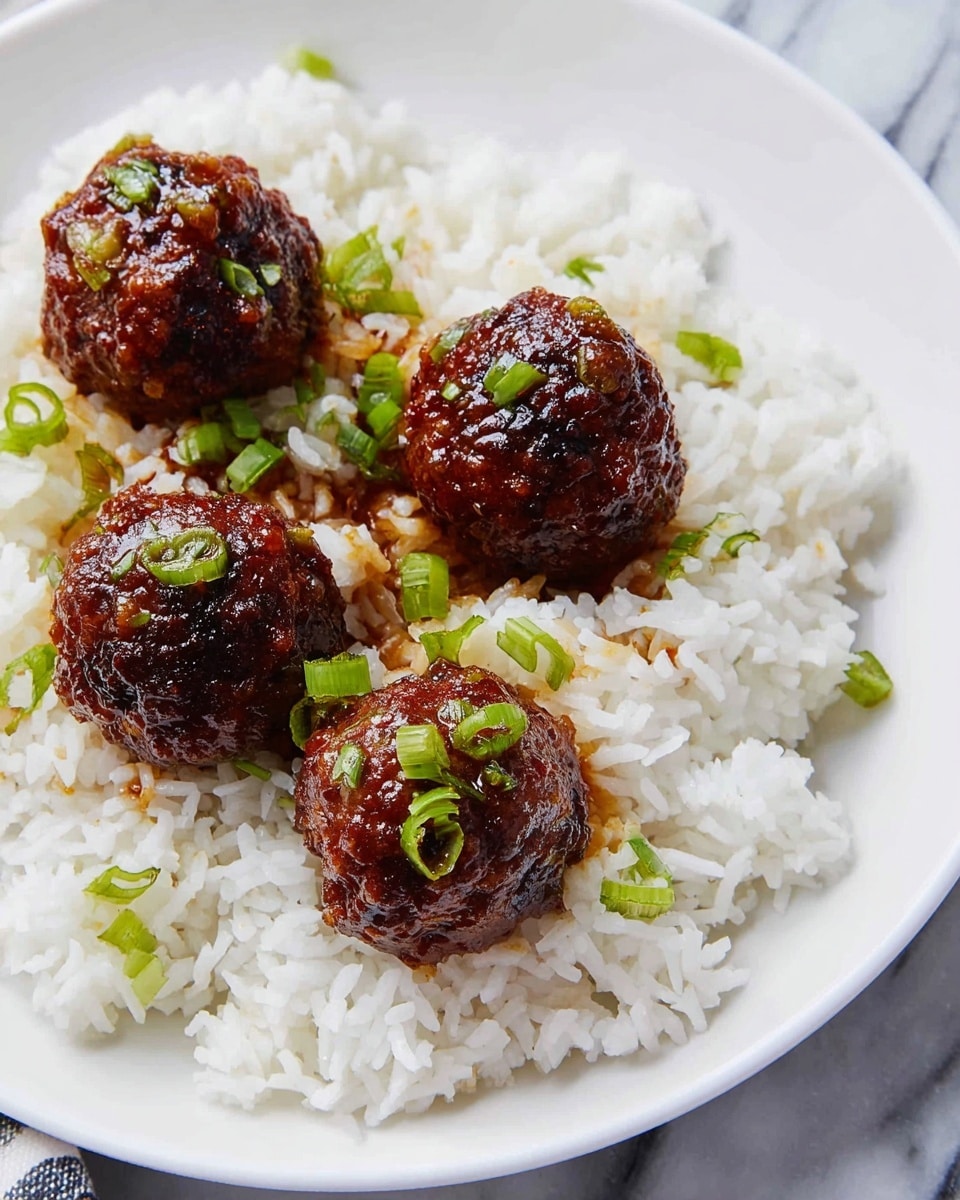 A white plate holds a bed of white steamed rice as the bottom layer, soft and flaky with individual grains visible. On top of the rice, four round meatballs are placed, each with a dark brown crispy texture and a glossy coating of sauce that shines under the light. Small green onion pieces are sprinkled on and around the meatballs, adding bright green spots of color. The plate rests on a white marbled surface with a slight pattern. photo taken with an iphone --ar 4:5 --v 7
