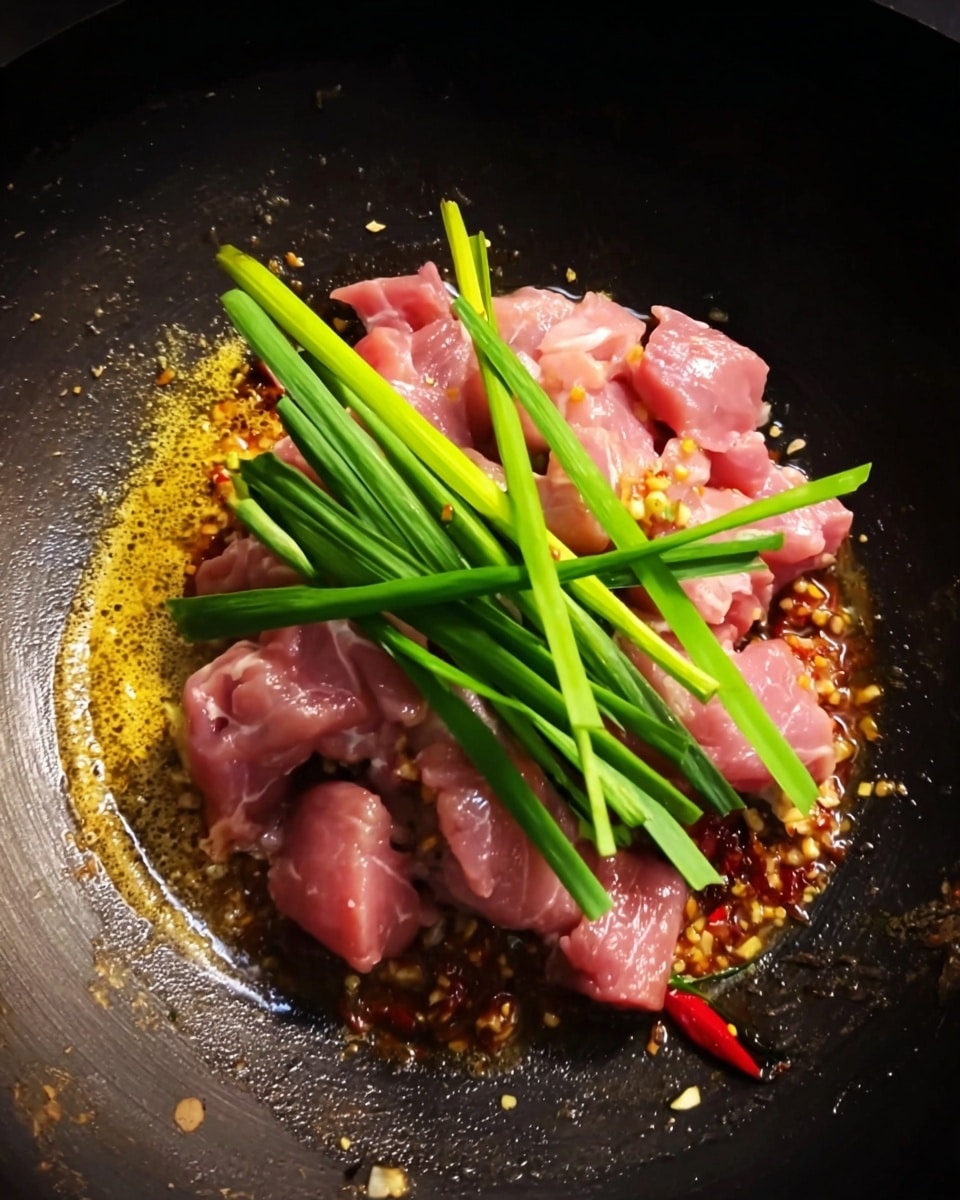 In a black cooking pan, there is a pile of raw pink meat pieces placed over a golden yellow and red spicy mixture at the bottom. On top of the meat, several bright green spring onion stalks are laid, crossing each other in different directions. The pan has dark edges with some signs of use and wear, showing a rough texture. photo taken with an iphone --ar 4:5 --v 7