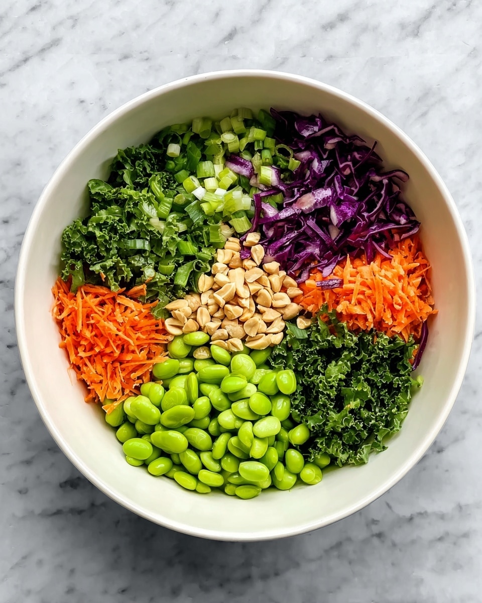 A white bowl holds six neat sections of fresh ingredients arranged in a circle, each showing a different bright color and texture. Starting from the bottom left and moving clockwise: a pile of smooth, shiny green edamame beans, next a mound of fine, bright orange grated carrots, followed by small light green slices of scallions. Above these are small pieces of chopped dark purple cabbage, then finely chopped fresh green herbs, and curly dark green kale leaves. In the middle of the bowl sits a small pile of light tan roasted peanuts. The bowl is placed on a white marbled surface. Photo taken with an iphone --ar 4:5 --v 7