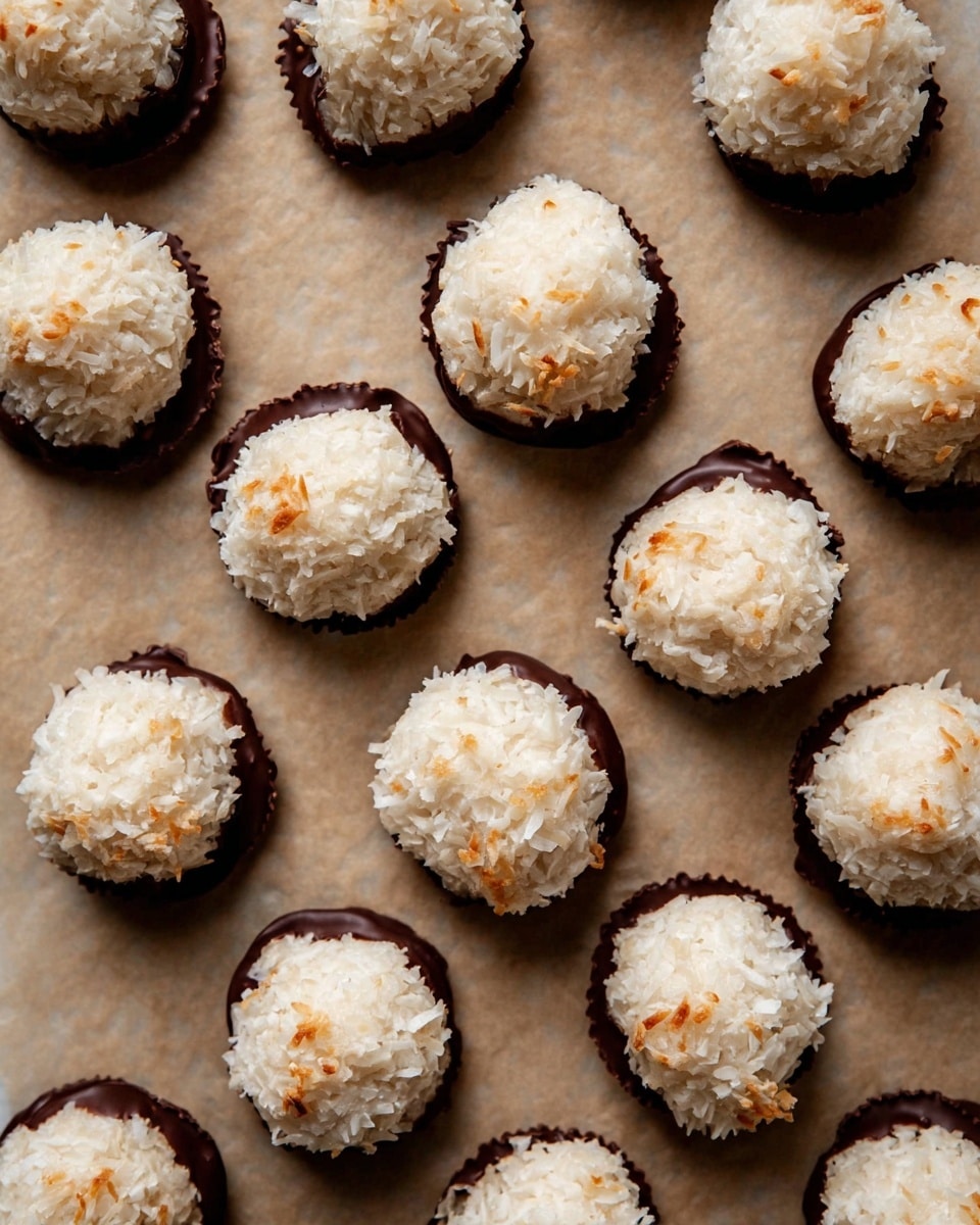 The image shows many small round treats arranged neatly on a light brown baking paper with a white marbled texture background. Each treat has two layers: the bottom layer is a dark, glossy chocolate base with uneven edges, and the top layer is a fluffy, textured white coconut ball with some light golden toasted spots. The treats are placed close but not touching each other, showing a clear contrast between the smooth dark chocolate and the rough white coconut. photo taken with an iphone --ar 4:5 --v 7