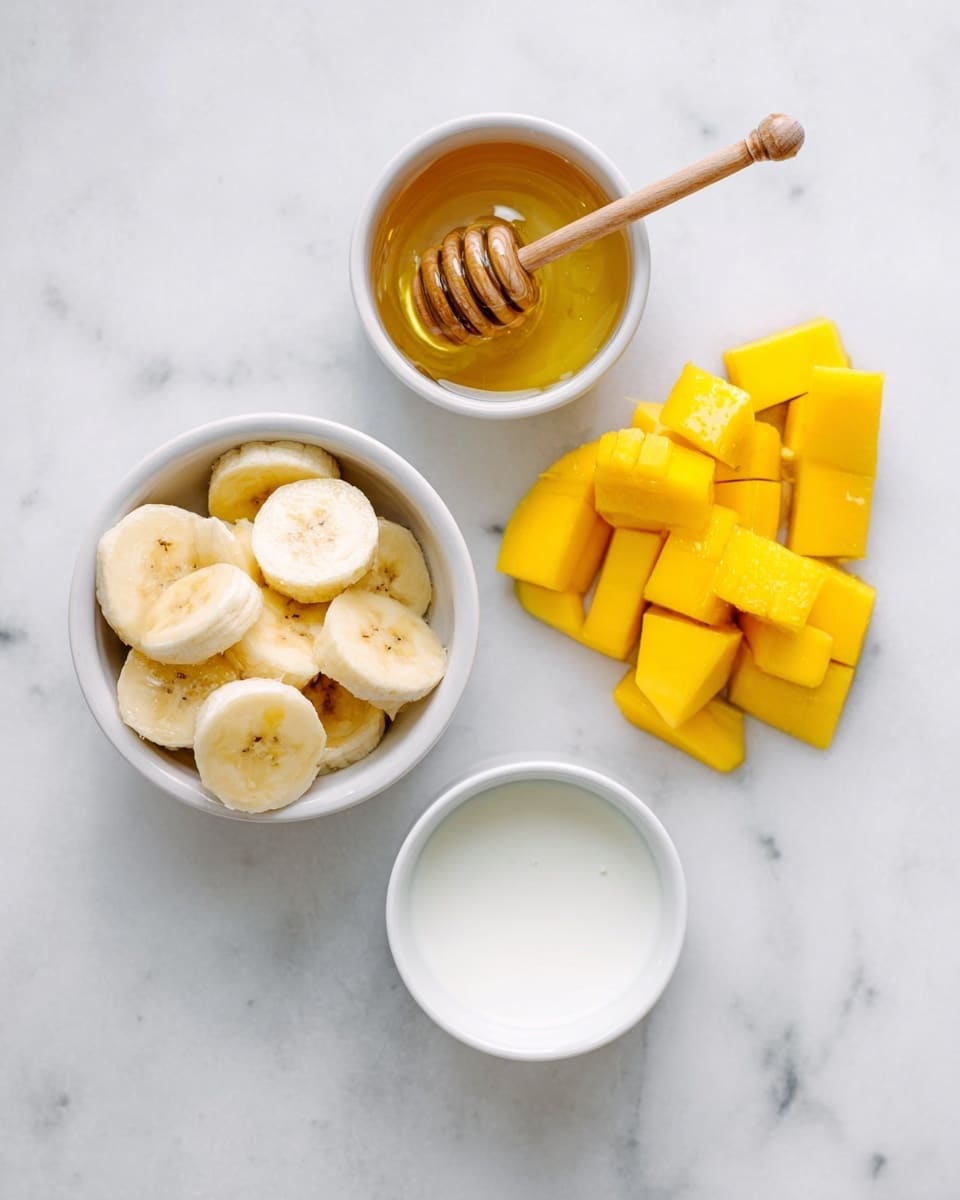 The image shows a white marbled surface with three small white bowls and a pile of cut yellow mango pieces arranged in a triangular shape. The top left bowl contains golden honey with a wooden honey dipper resting inside. The bottom left bowl holds round banana slices that are light yellow with a soft texture. The bottom right bowl is filled with a white liquid, likely milk. The mango pieces are bright yellow and juicy, placed loosely next to the bowls. photo taken with an iphone --ar 4:5 --v 7