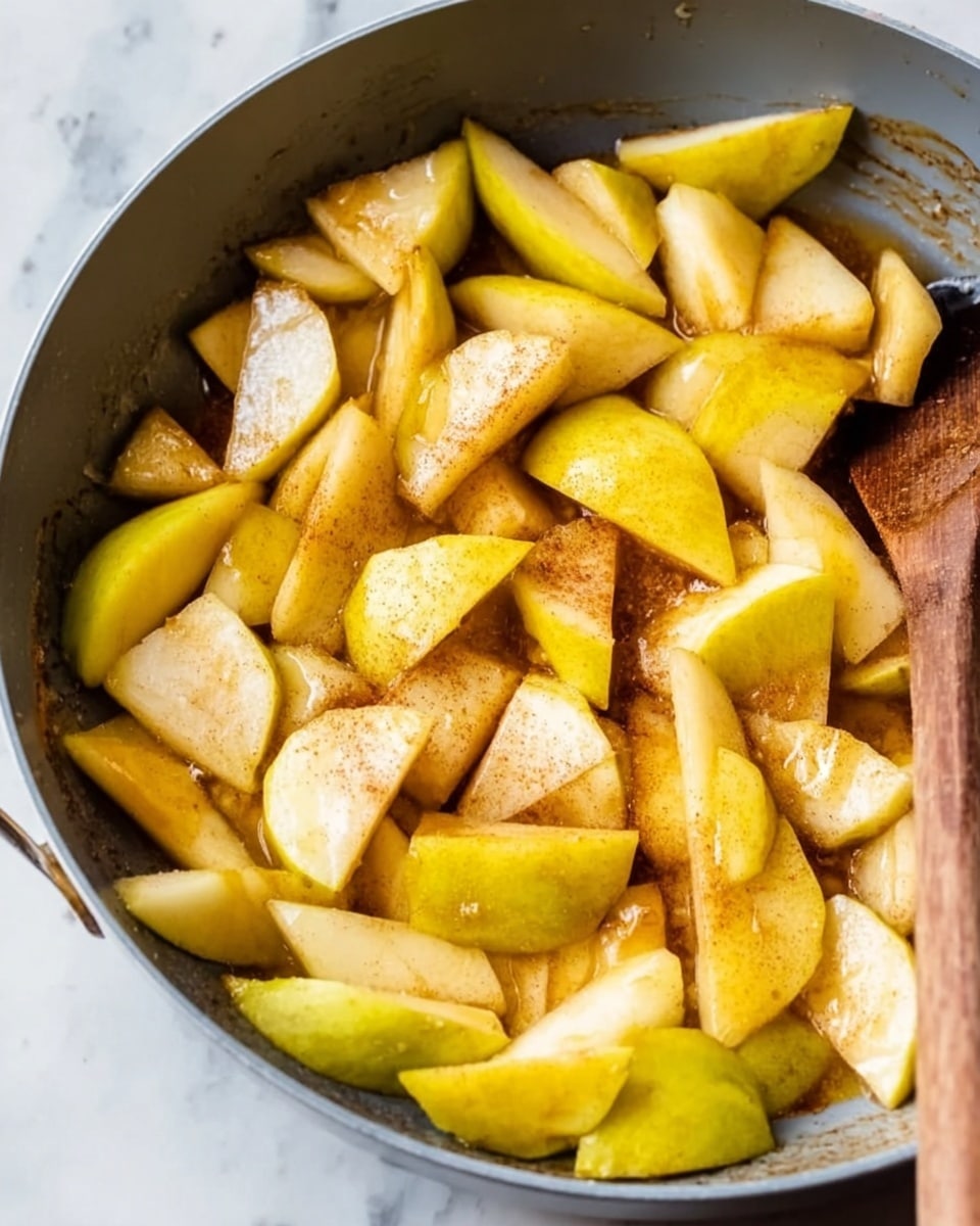 The image shows a close-up of a gray pan filled with many pieces of sliced yellow apples and pears. The fruit pieces have different shapes and sizes, some are thin wedges while others are chunkier, with a light brown powder sprinkled on top. A wooden spoon is seen resting inside the pan at the bottom right corner. The pan sits on a white marbled surface. photo taken with an iphone --ar 4:5 --v 7
