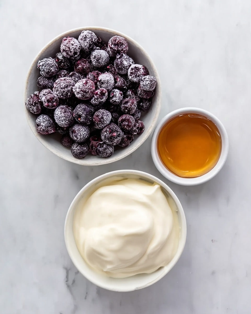 The image shows three white bowls on a white marbled surface. The top left bowl contains many dark purple frozen berries with a light layer of frost. To the right, another bowl holds smooth, creamy white yogurt. Below the berries, there is a small bowl filled with amber-colored honey. The bowls are arranged neatly, making a simple and clean composition. Photo taken with an iphone --ar 4:5 --v 7