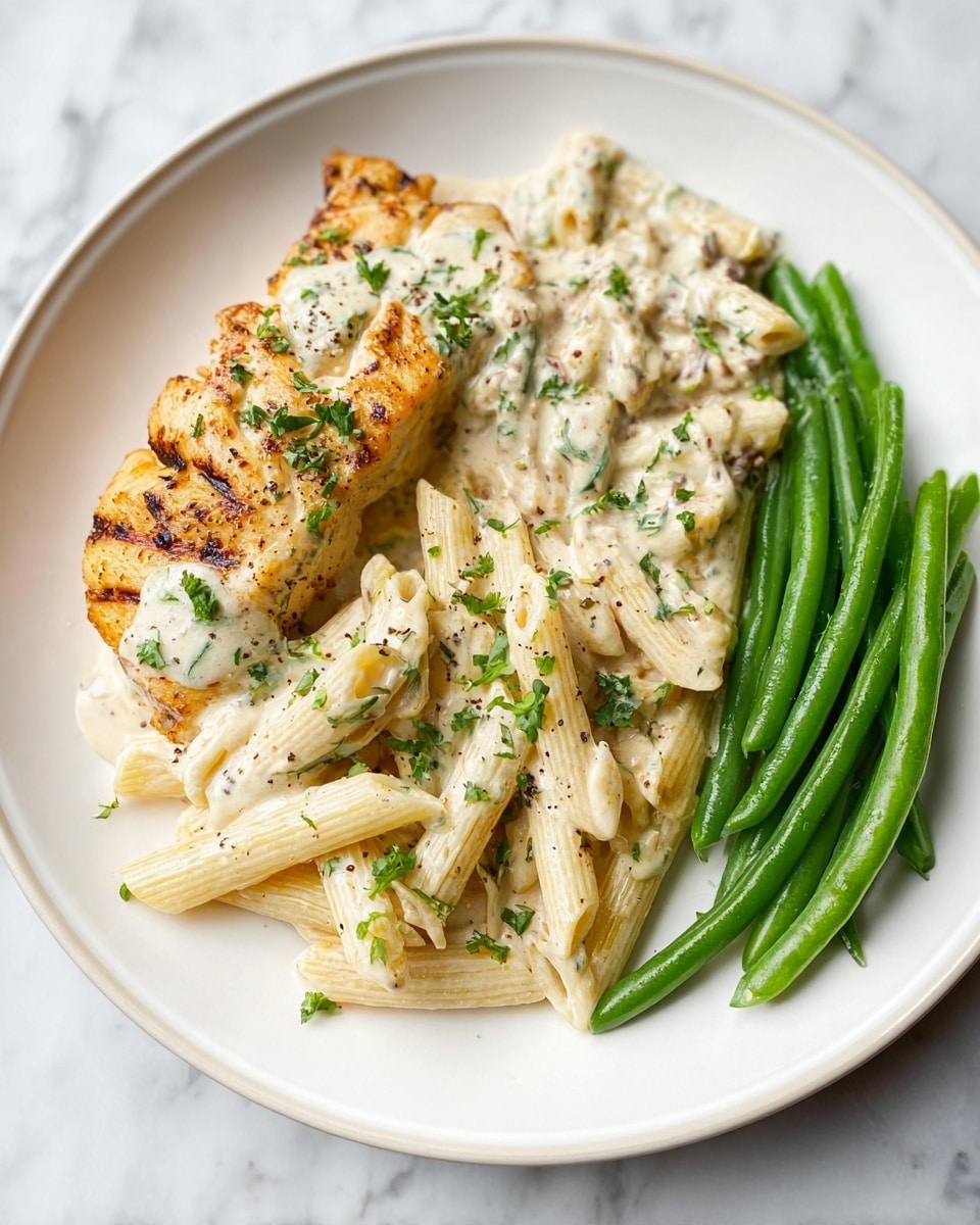 The dish is served on a white round plate placed on a white marbled surface. It has three main parts: on the left, a piece of golden grilled fish with a slight shine and light grill marks, topped and surrounded by a creamy white sauce with green herb bits. In the middle-front, there is a generous portion of penne pasta, coated in the same creamy white herb sauce, with visible small pieces of onion and sprinkled with chopped green herbs and black pepper. On the right, bright green steamed green beans are placed neatly in a row, with subtle glistening and a light pepper seasoning. The colors contrast nicely: golden fish, creamy white pasta, and fresh green beans. photo taken with an iphone --ar 4:5 --v 7