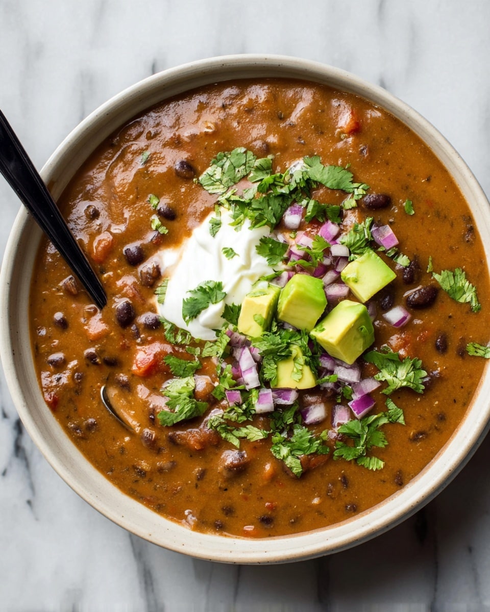 A creamy, thick brown bean soup fills a round white bowl, speckled with small black beans and bits of red tomato mixed evenly throughout. On top, there is a dollop of smooth white sour cream placed slightly off-center. Around and on the sour cream, small cubes of light green avocado provide fresh color, along with bright green cilantro leaves and finely chopped purple onion scattered across the soup’s surface. A black spoon rests inside the bowl, partially dipped into the soup on the left side. The bowl sits on a white marbled surface. photo taken with an iphone --ar 4:5 --v 7