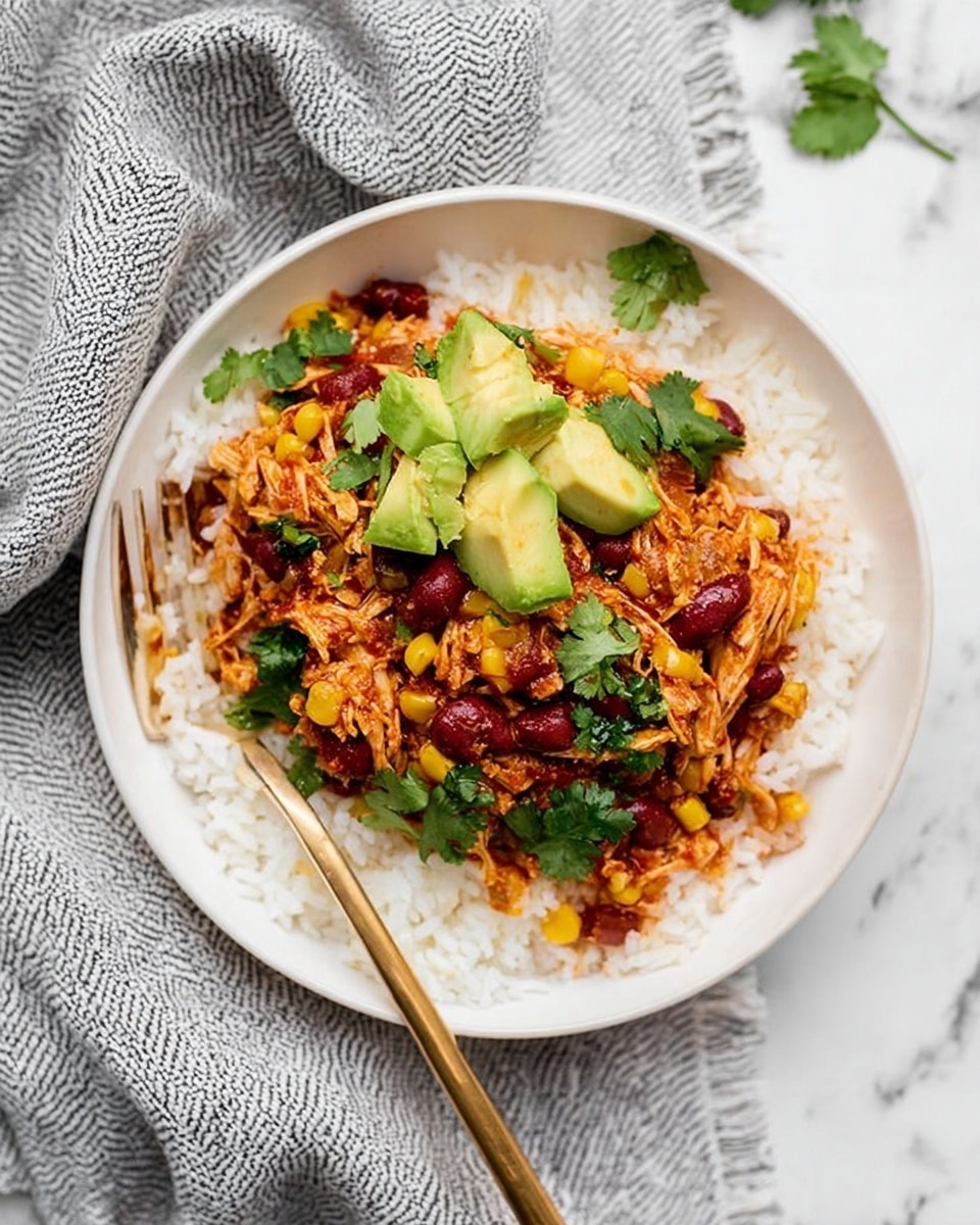 A white bowl is filled with a base layer of white rice. On top of the rice, there is a colorful mix of shredded chicken cooked with red kidney beans, yellow corn, and small pieces of tomatoes, giving a reddish-orange look with speckles of yellow and red. Fresh green cilantro leaves are scattered over the chicken mix, and there are several chunks of bright green avocado placed on top. A detailed gold fork is resting inside the bowl, on the left side. The bowl is set on a white marbled surface with a textured gray and white striped cloth partially underneath. photo taken with an iphone --ar 4:5 --v 7