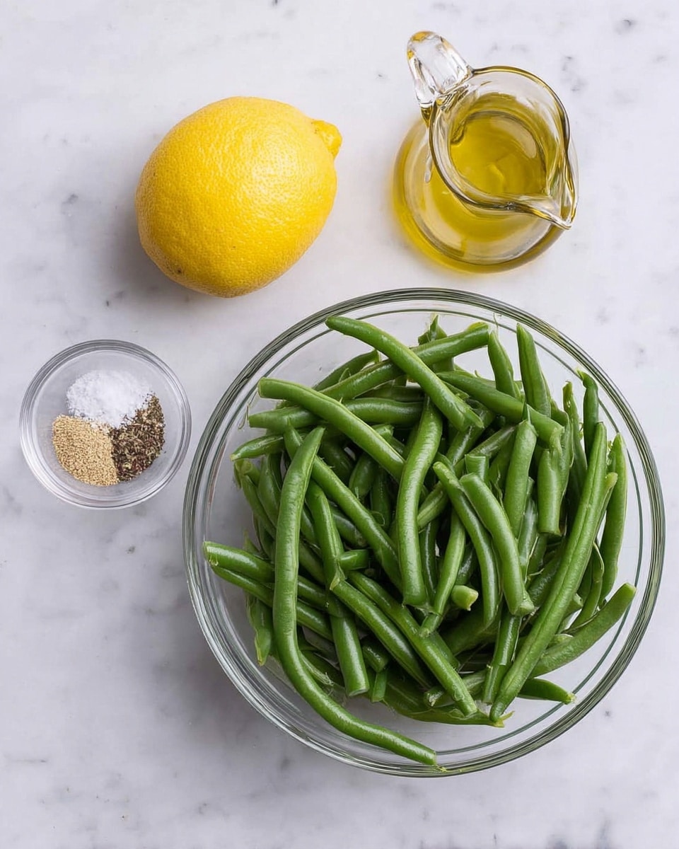 A clear glass bowl filled with fresh green beans is placed on a white marbled surface. To the left of the bowl lies a whole bright yellow lemon, next to a small clear glass dish containing coarse salt and ground black pepper. Above the lemon is a small glass container of olive oil with a glass spout. The colors are fresh and natural, showing vibrant green, bright yellow, and transparent glass textures, all set against the smooth white marbled background. Photo taken with an iphone --ar 4:5 --v 7